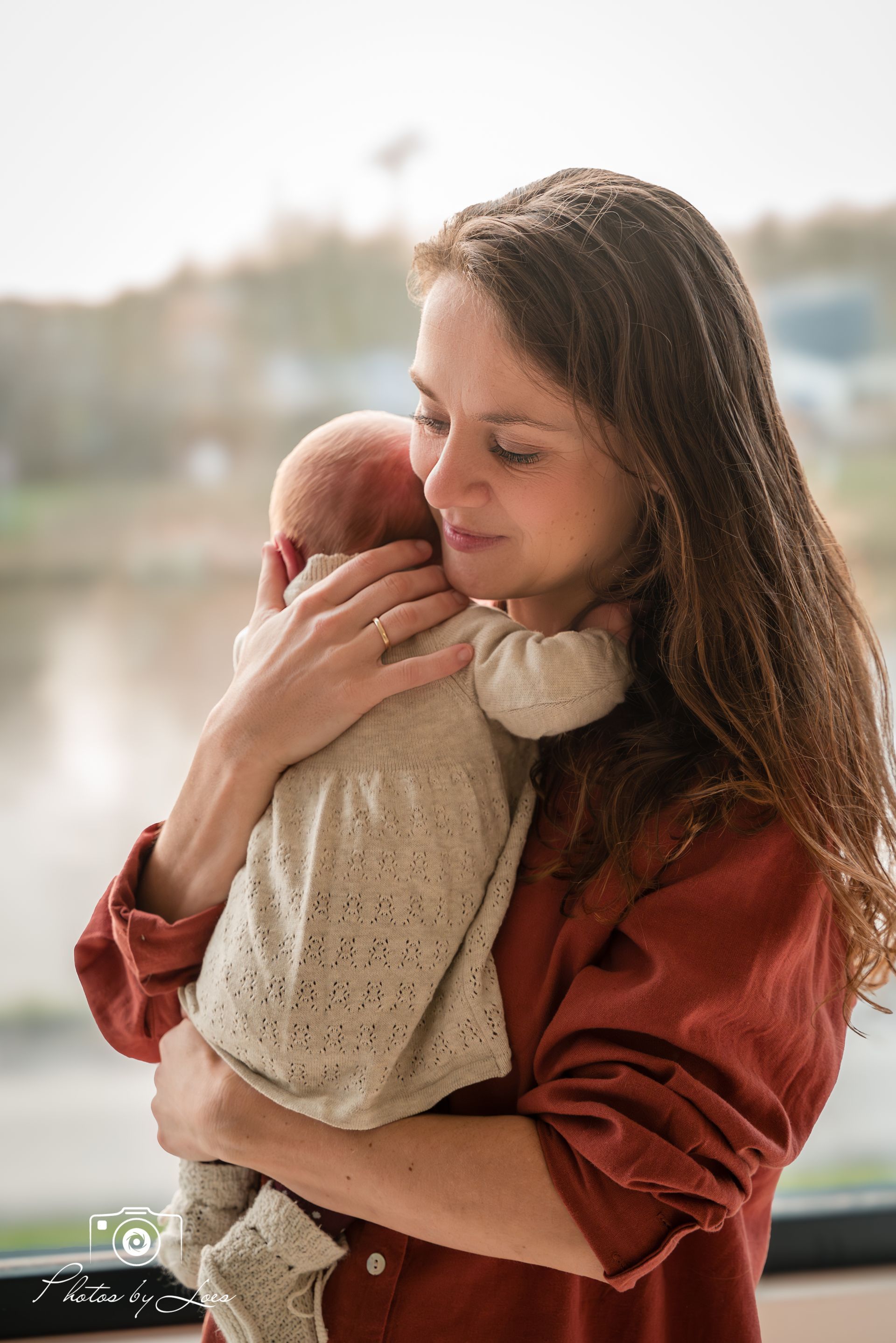 Een vrouw houdt een pasgeboren baby in haar armen voor een raam.