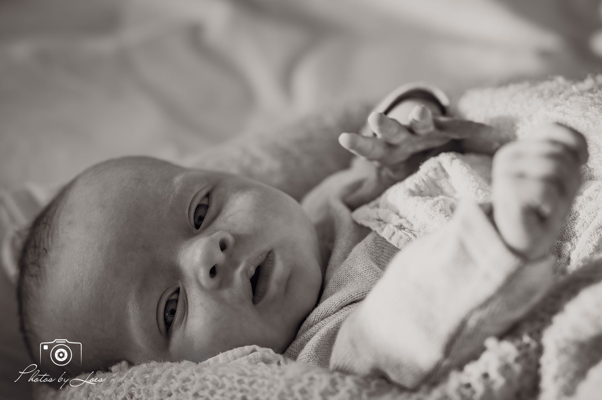 Een zwart-witfoto van een baby die op een deken ligt.