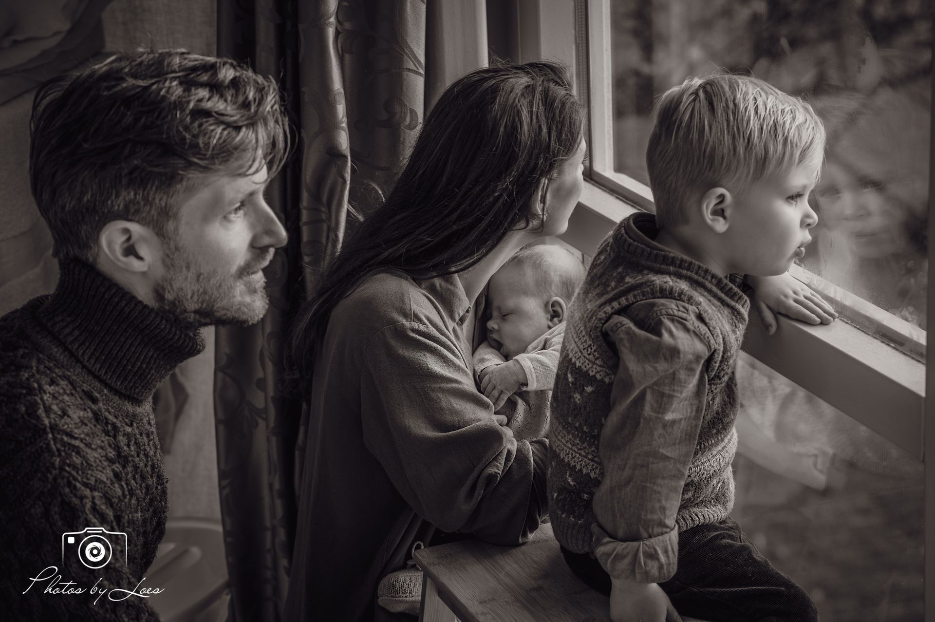 Een zwart-witfoto van een gezin dat uit een raam kijkt.