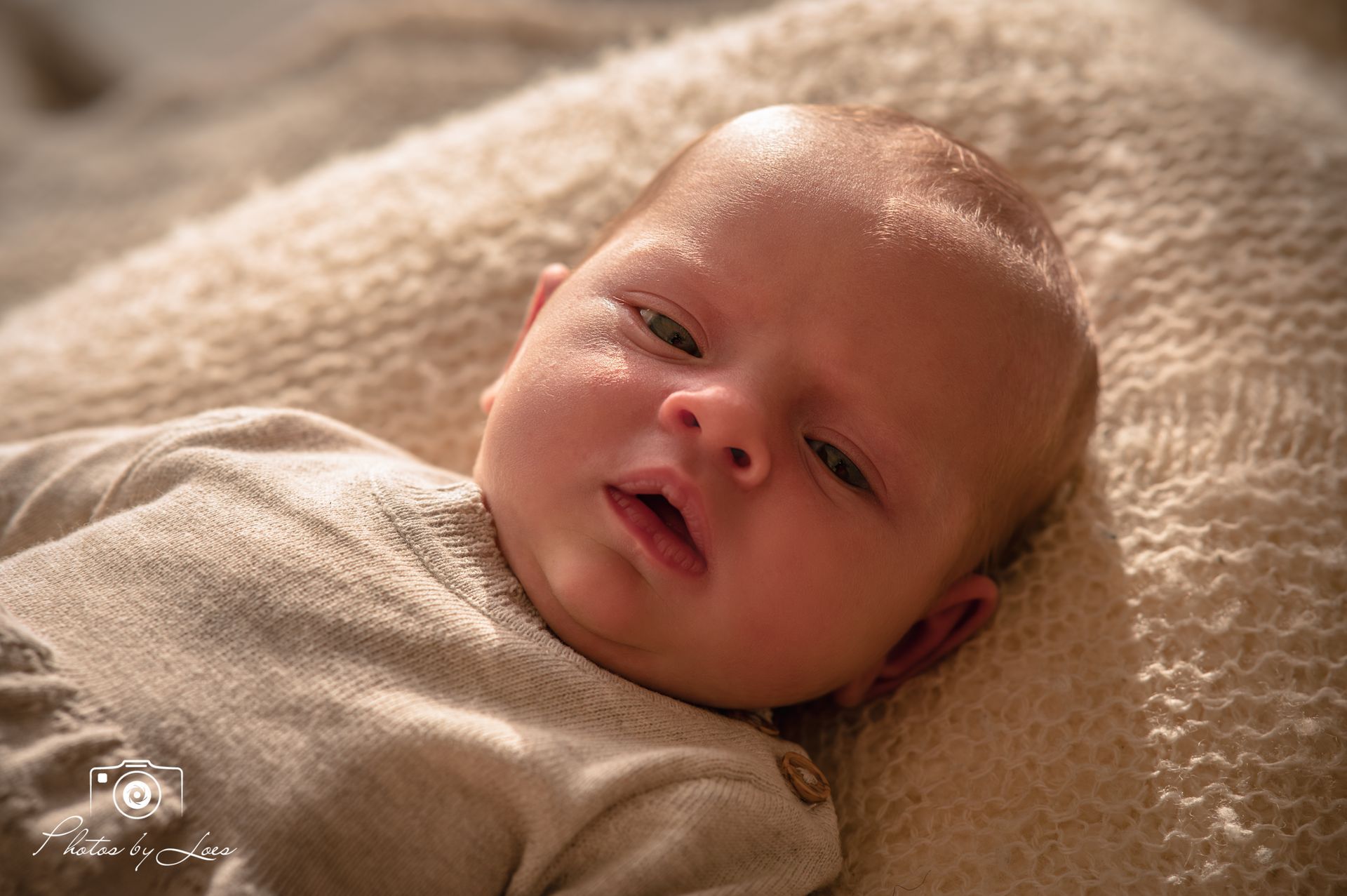 Een baby ligt op een deken en kijkt naar de camera.