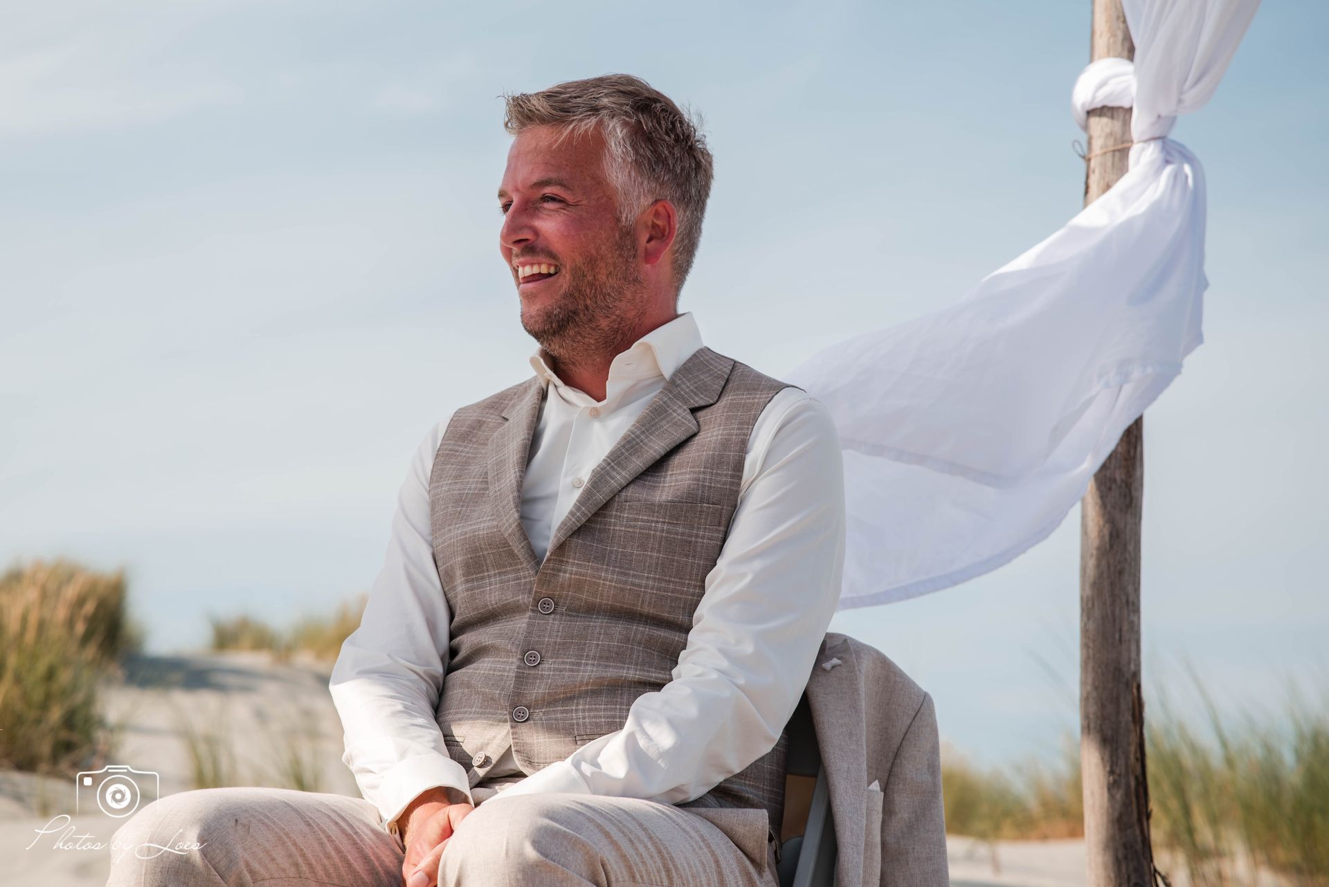 Een man in pak zit op een stoel op het strand.