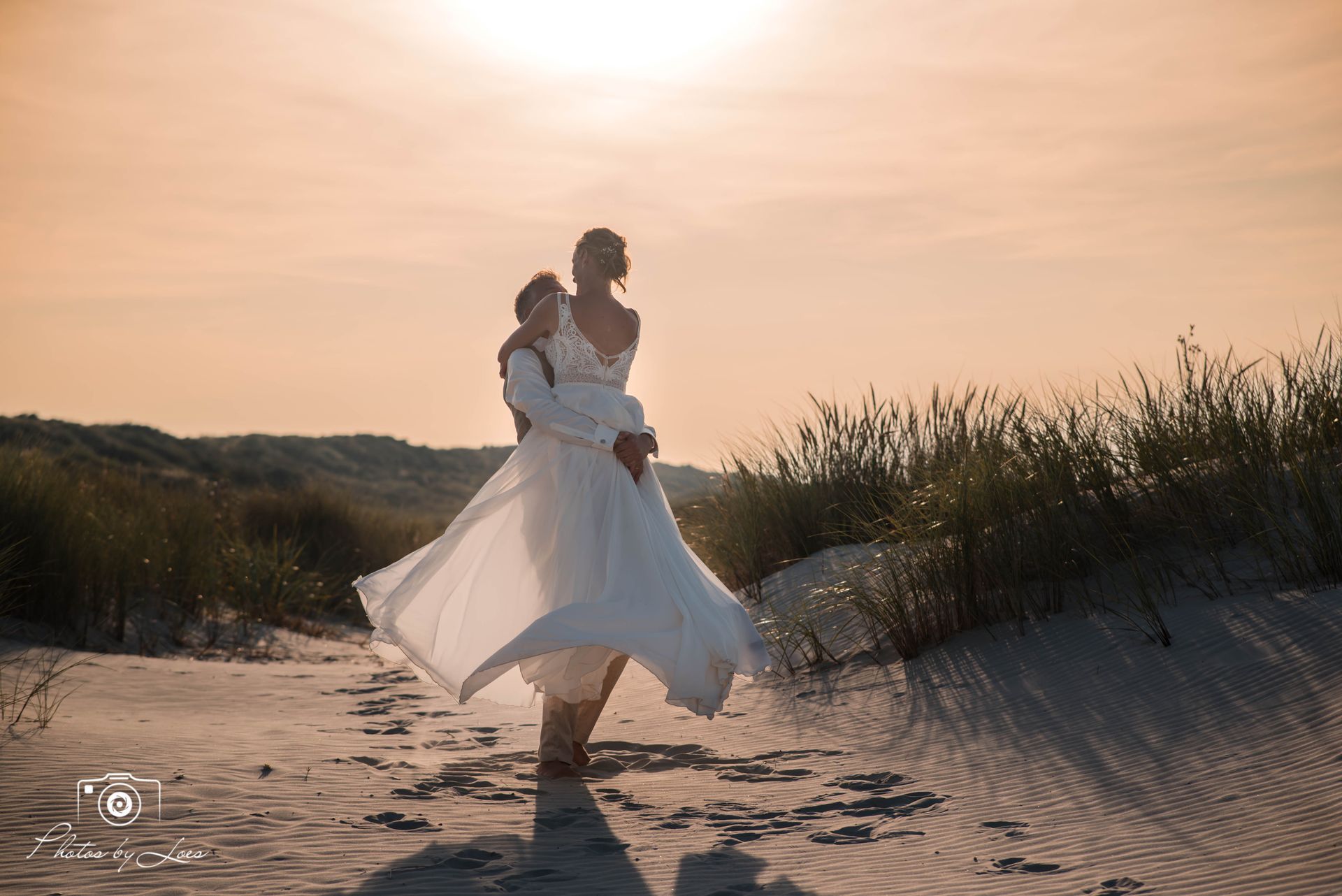 Een bruid en bruidegom dansen op het strand bij zonsondergang.