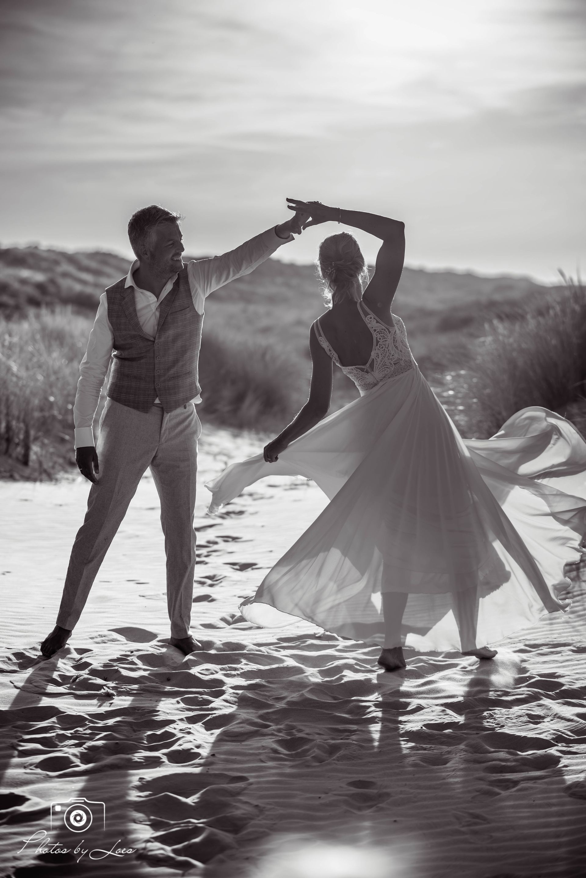 Een zwart-witfoto van een bruid en bruidegom die dansen op het strand.