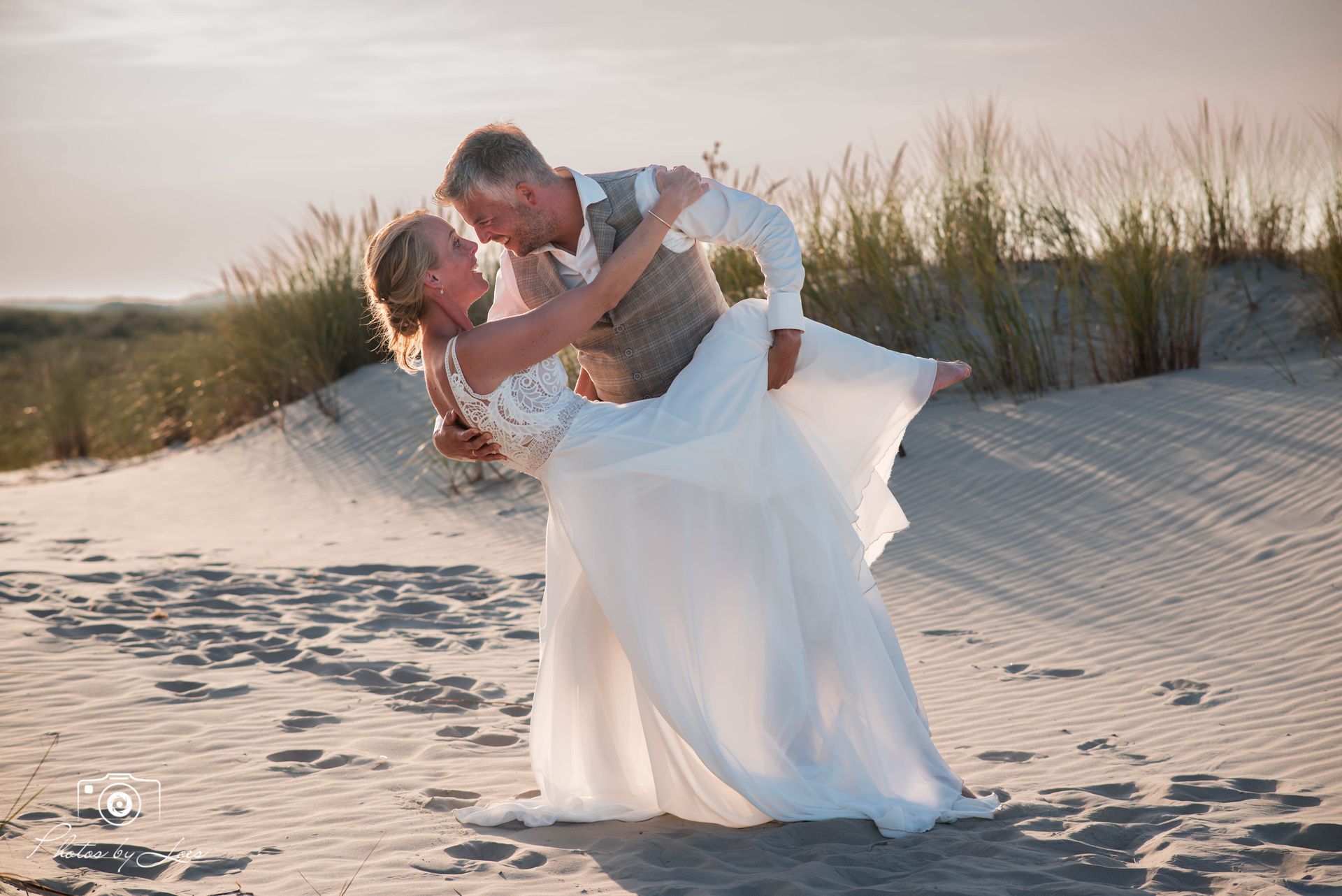 Een bruid en bruidegom dansen op het strand.