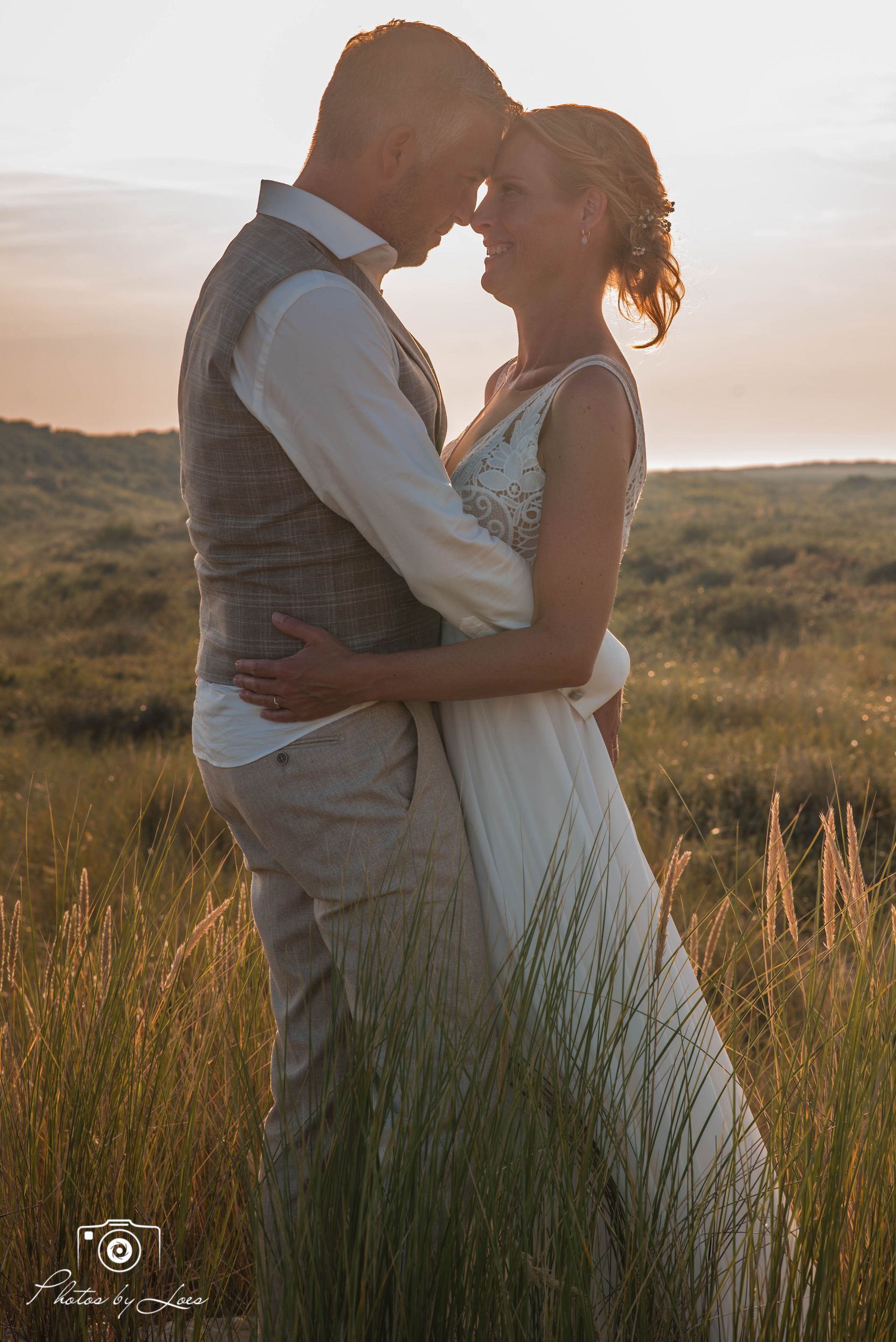 Een bruid en bruidegom omhelzen elkaar in een veld bij zonsondergang.