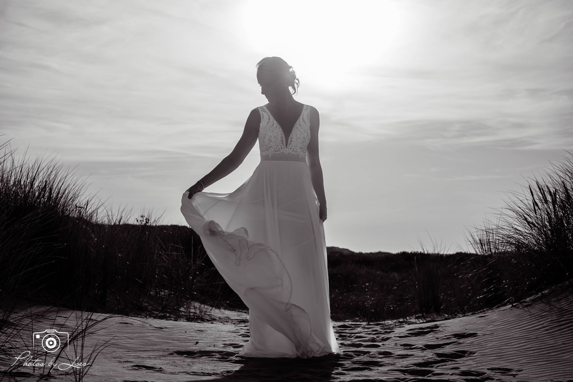 Een zwart-witfoto van een vrouw in een trouwjurk die op het strand staat.