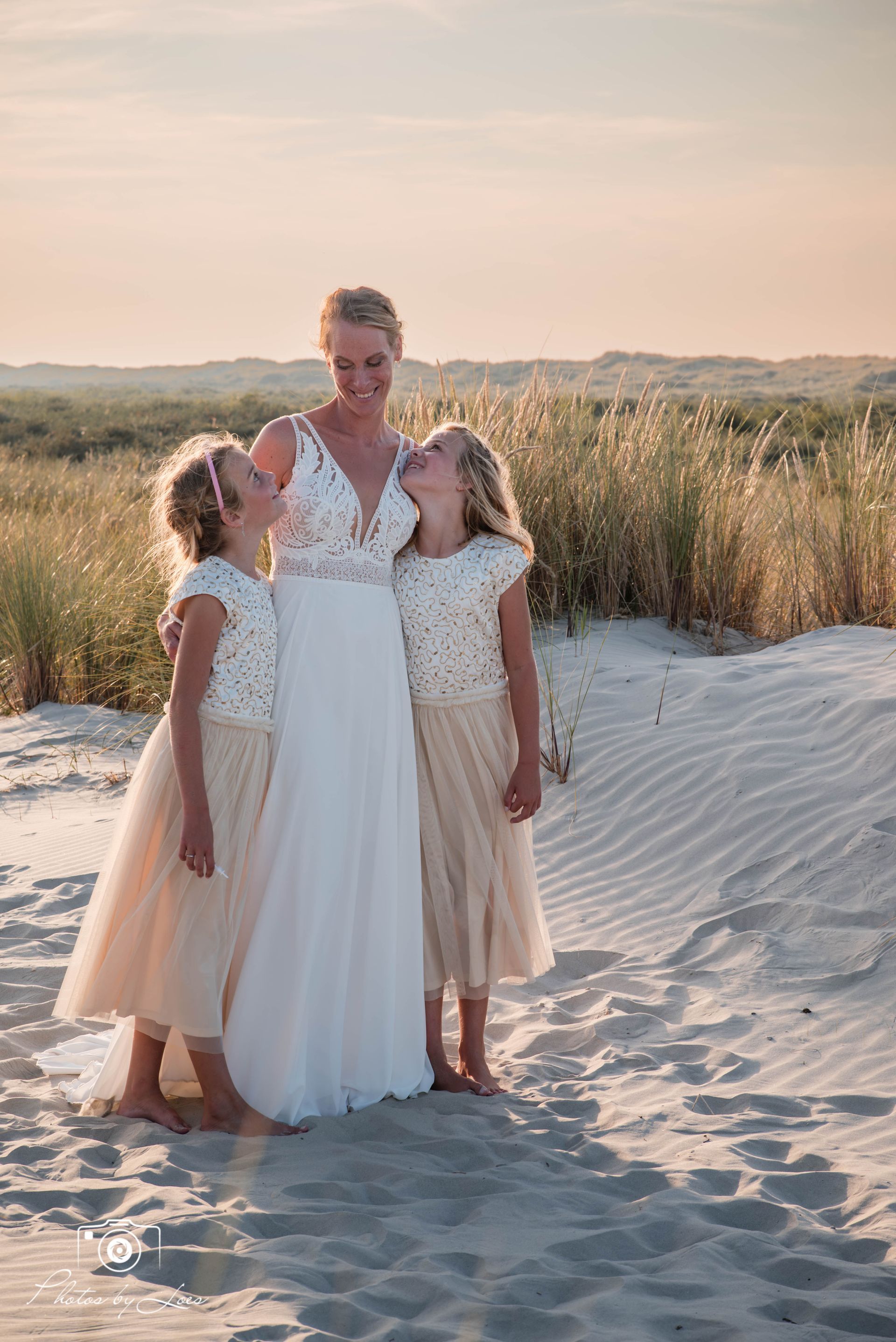 Een bruid en haar twee bloemenmeisjes poseren voor een foto op het strand.