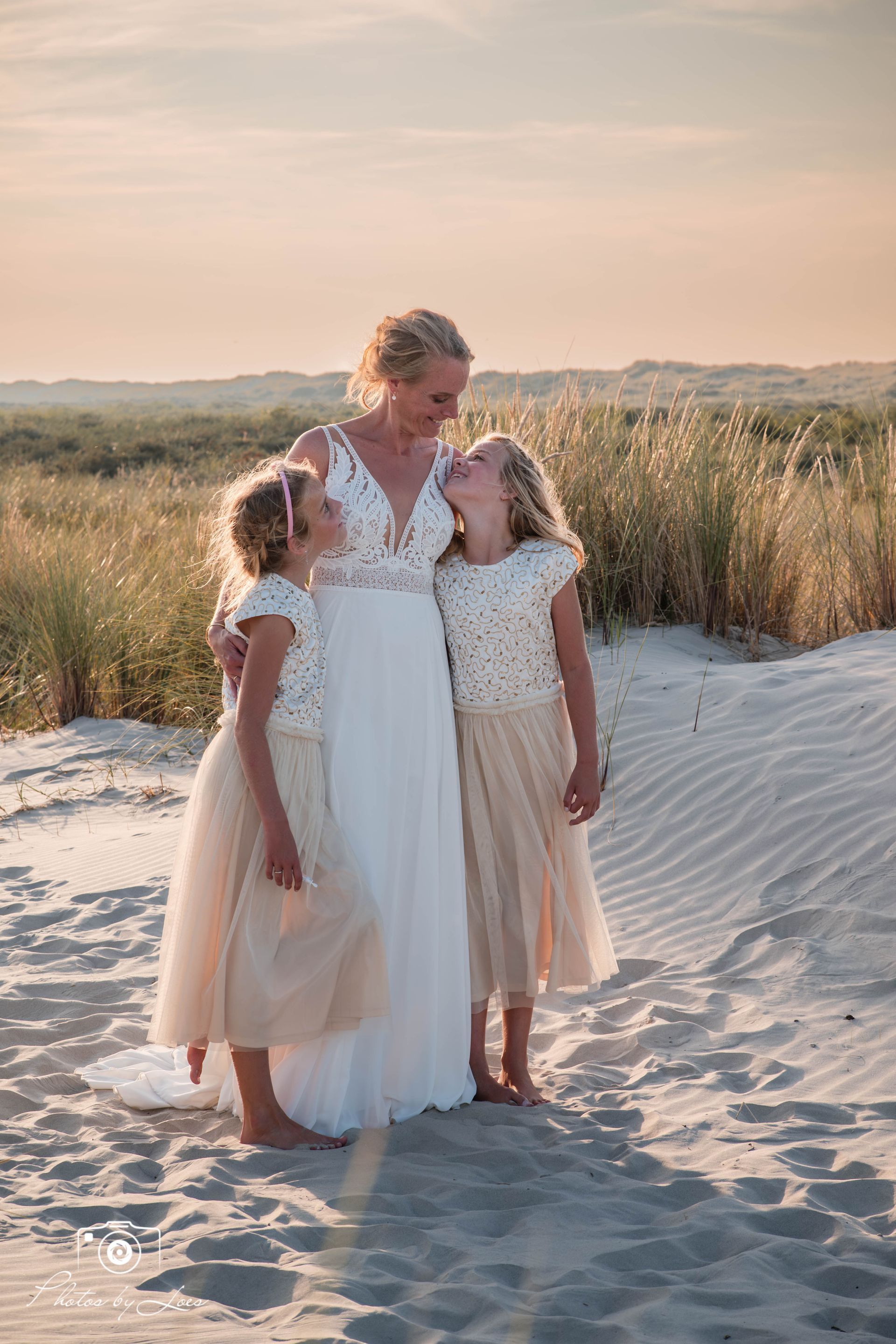 Een bruid en haar twee bloemenmeisjes staan ​​op een zandstrand.