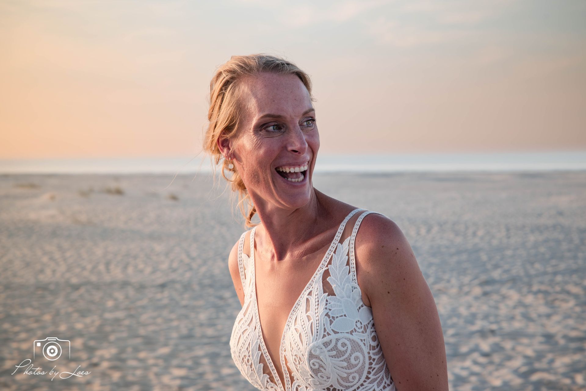Een vrouw in een trouwjurk lacht op het strand.