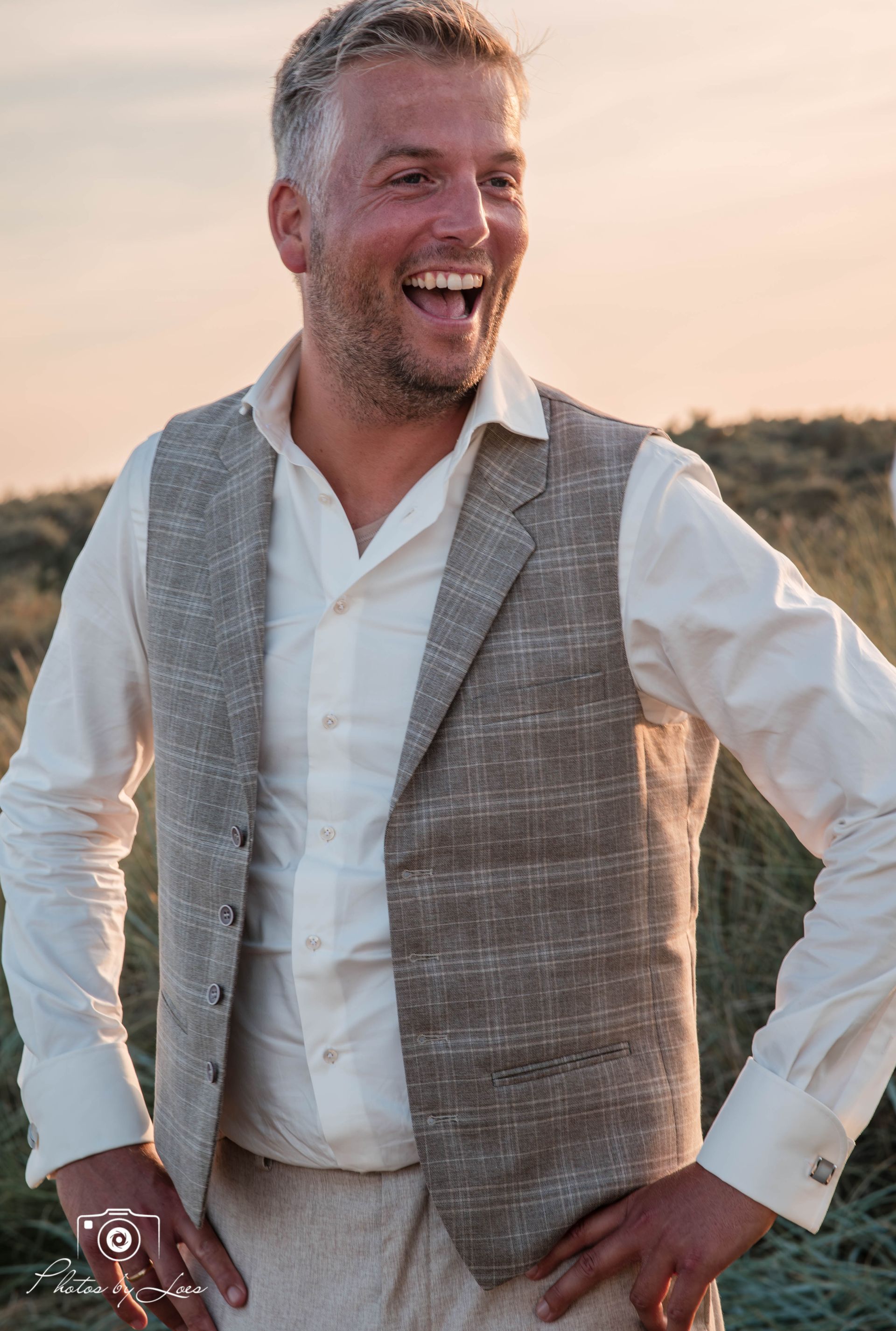 Een man met een vest en een wit overhemd staat in een veld.