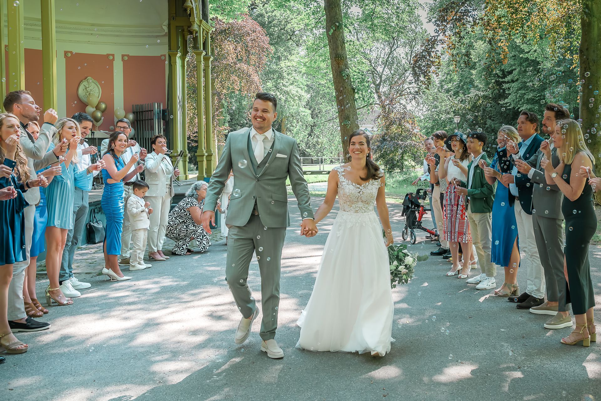 Een bruid en bruidegom lopen hand in hand door een menigte.