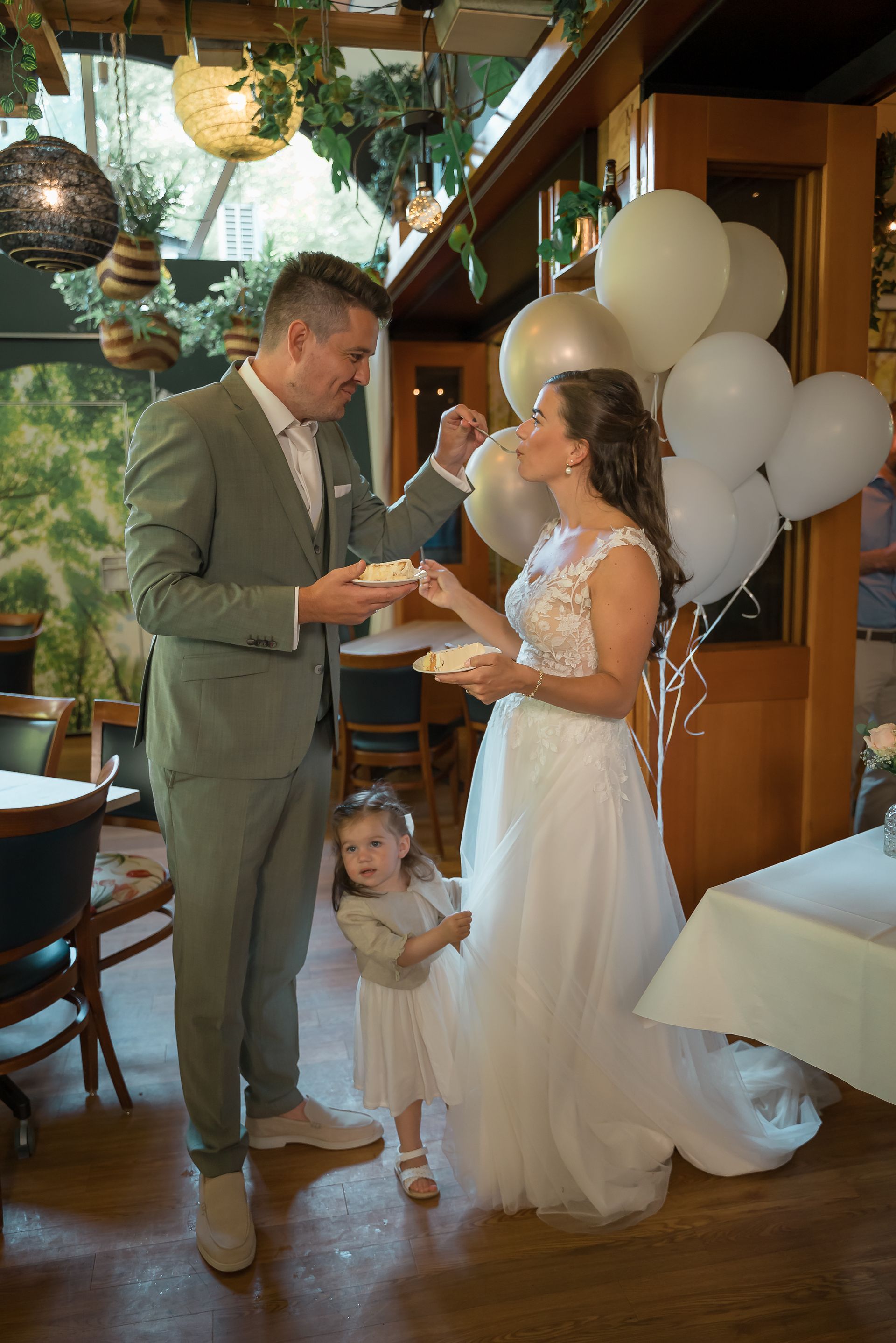 Een bruid en bruidegom snijden de bruidstaart aan met een klein meisje.