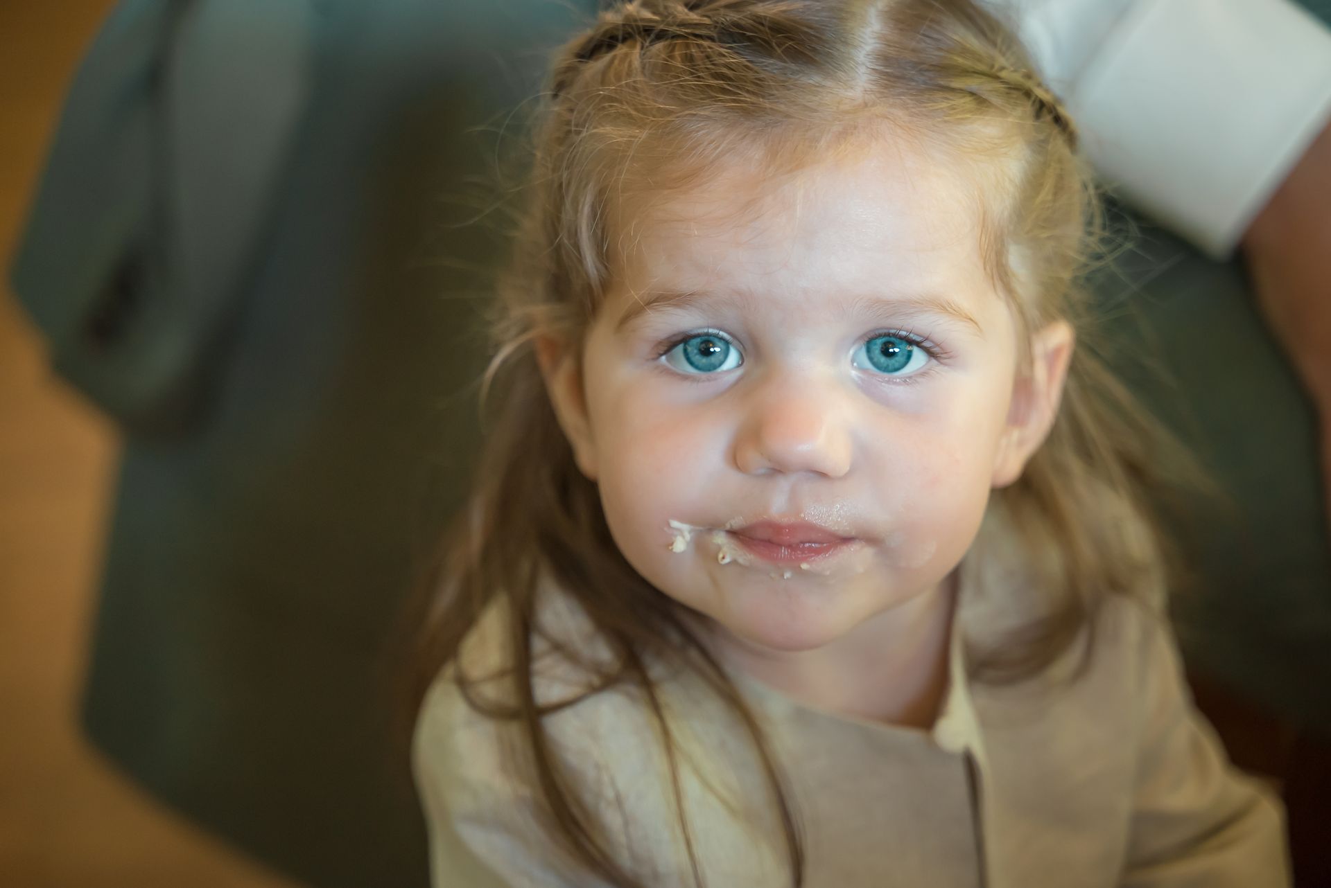 Een klein meisje met yoghurt op haar gezicht kijkt naar de camera.
