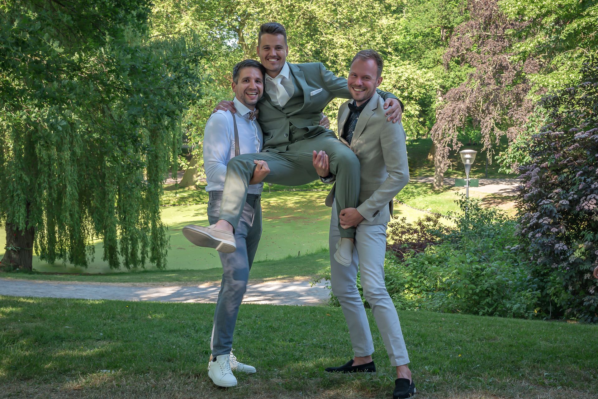 Twee mannen dragen een man in hun armen in een park.