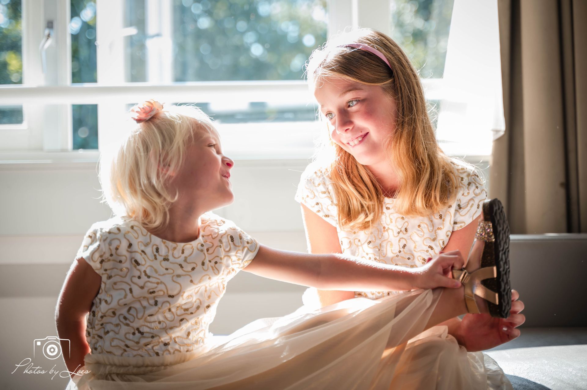 Twee kleine meisjes zitten naast elkaar voor een raam.