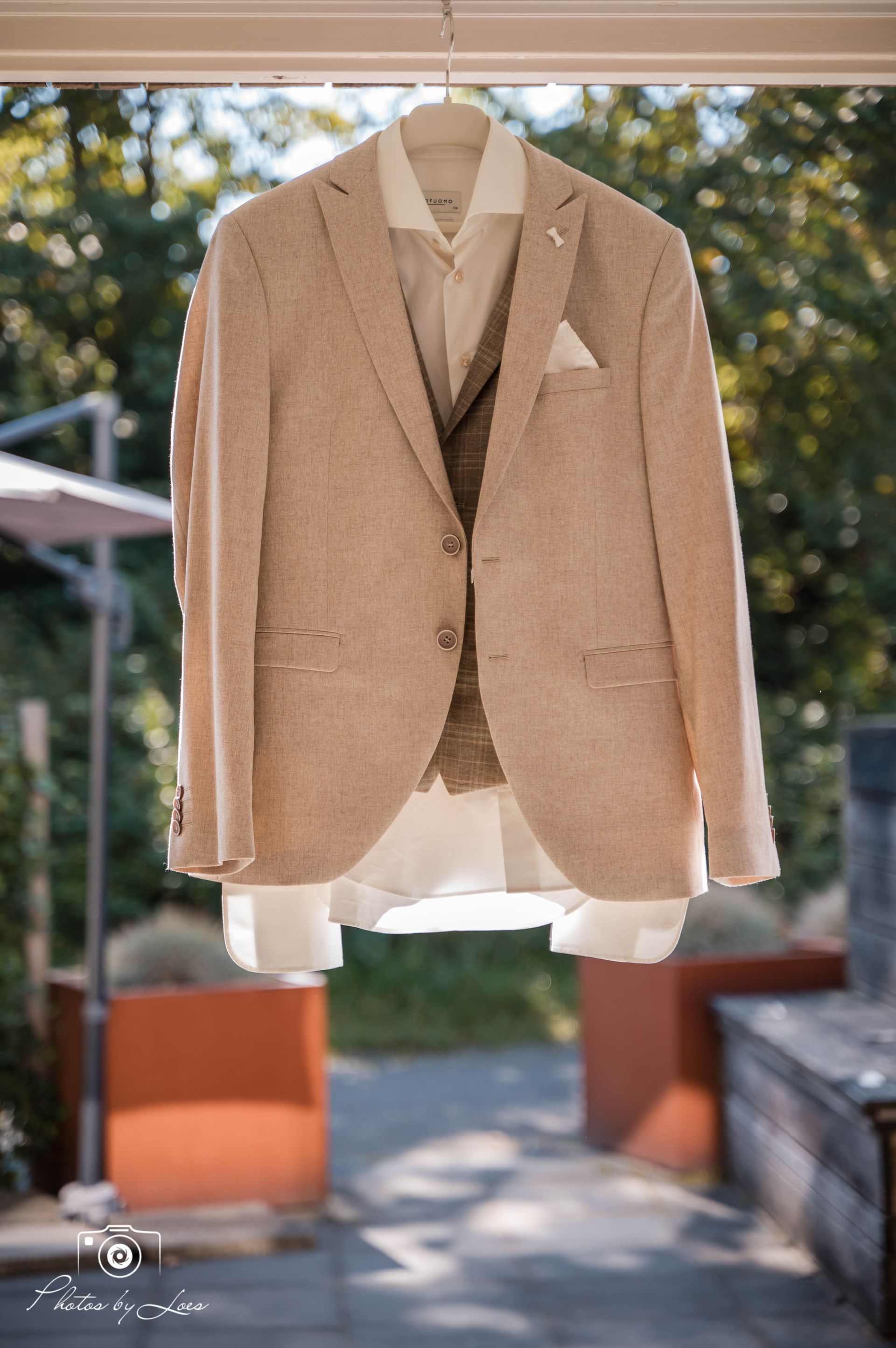 Een bruin colbert en een wit overhemd hangen aan een hanger.