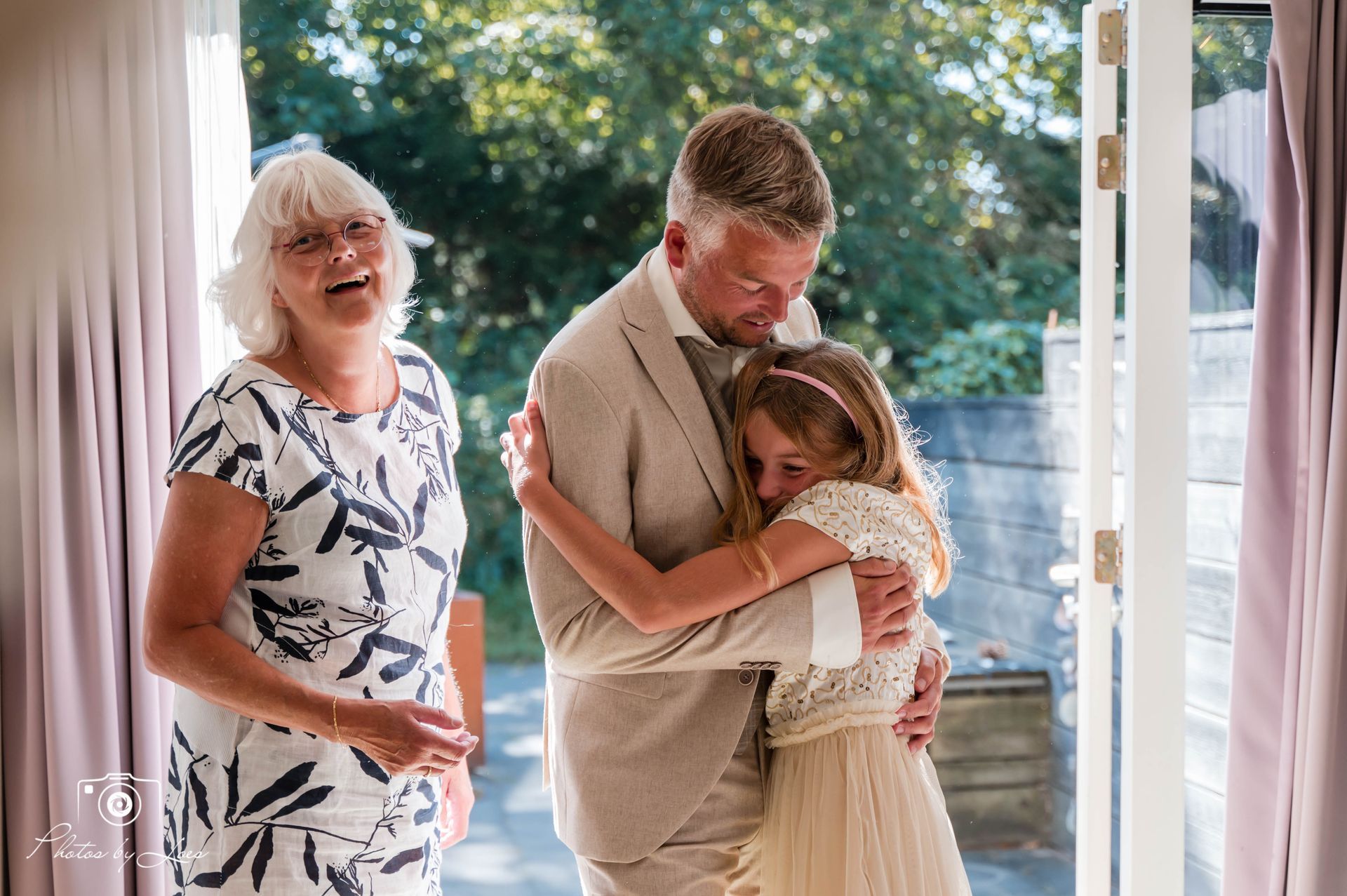 Een man en een vrouw omhelzen een klein meisje in een kamer.