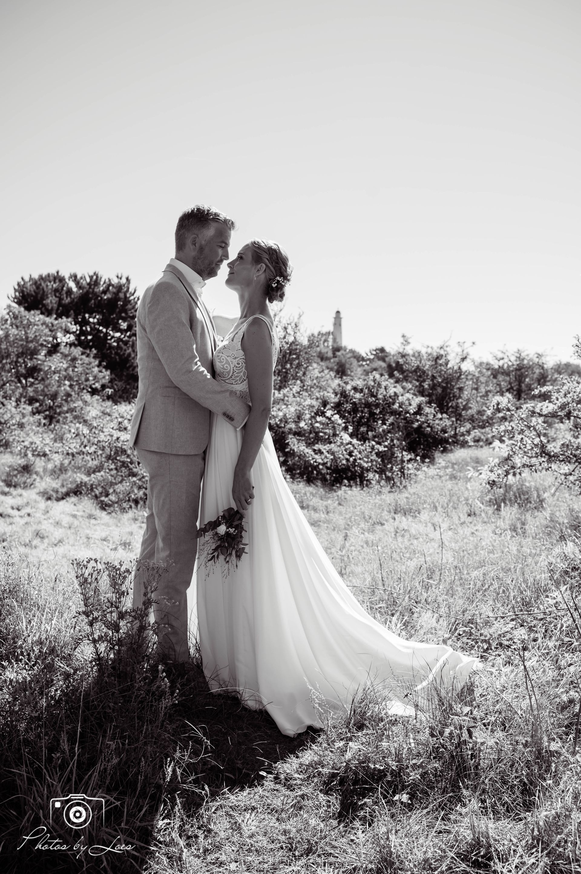 Een zwart-witfoto van een bruid en bruidegom die in een veld staan.