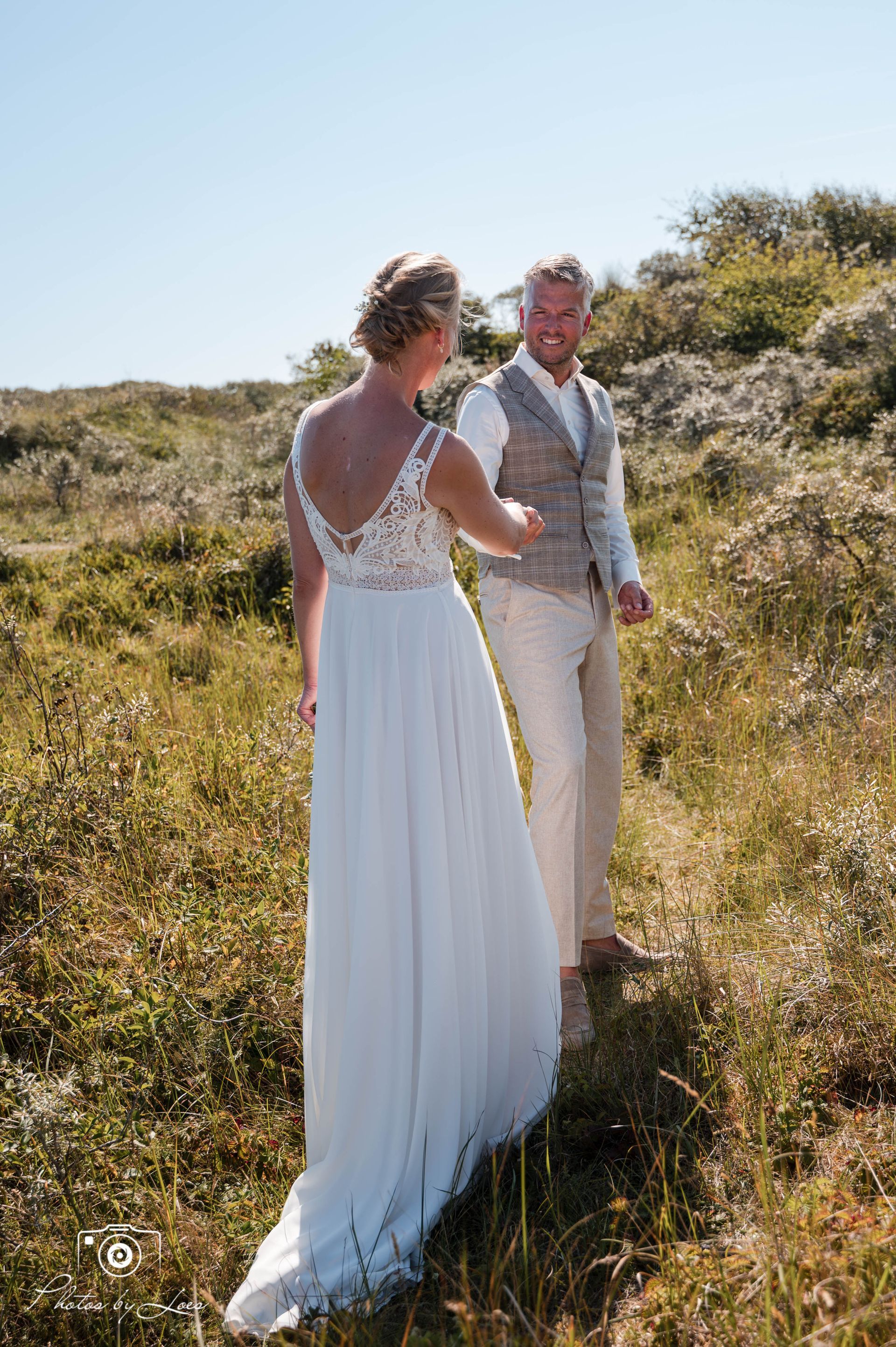 Een bruid en bruidegom staan ​​hand in hand in een veld.