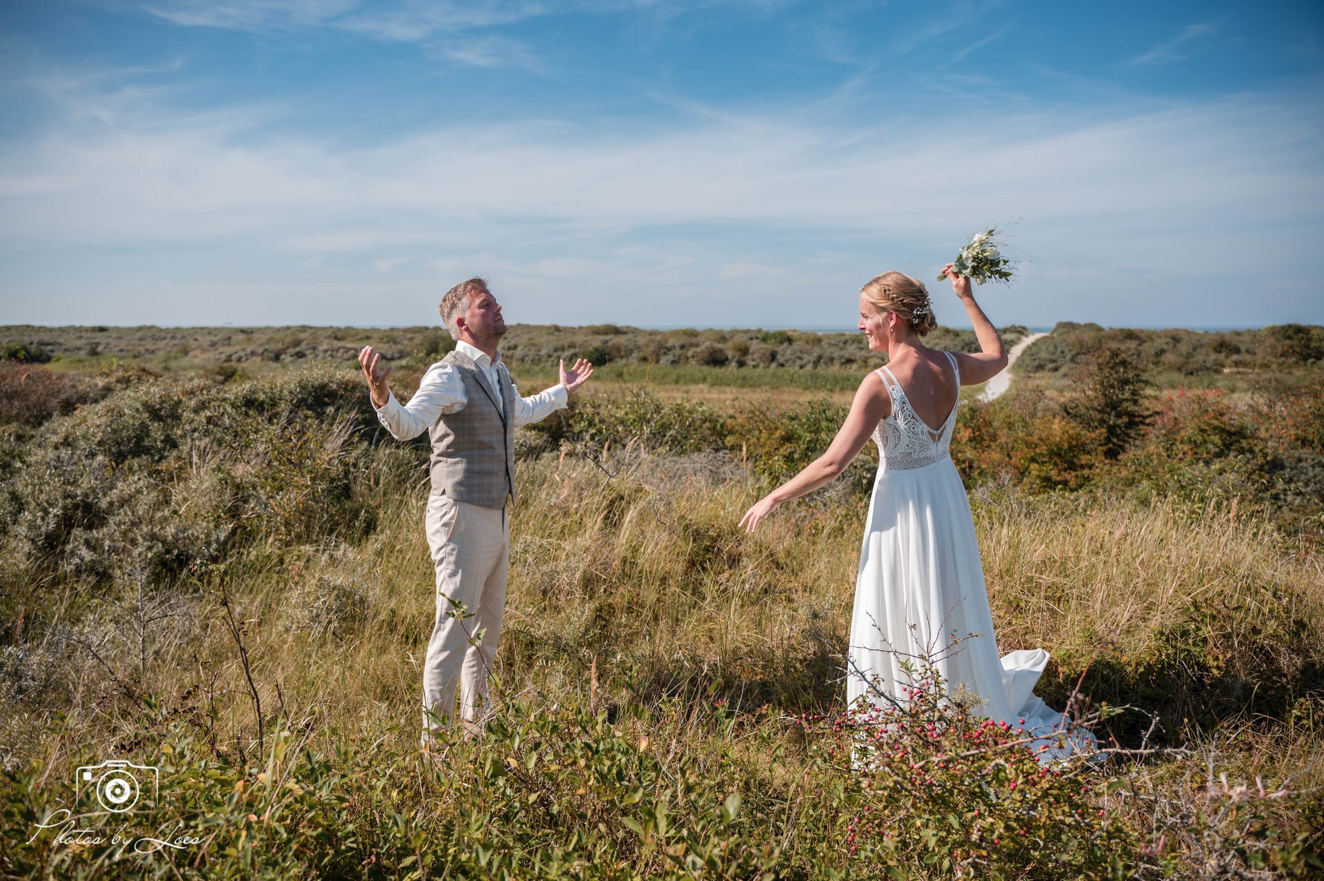 Een bruid en bruidegom staan ​​in een veld met hun armen uitgestrekt.