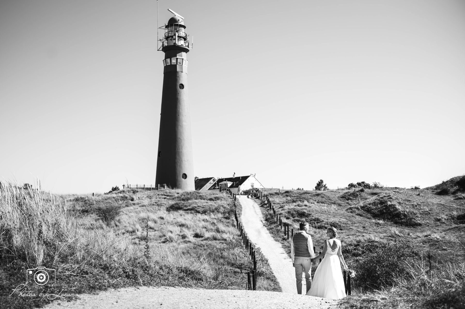 Een zwart-witfoto van een bruidspaar dat naar een vuurtoren loopt.