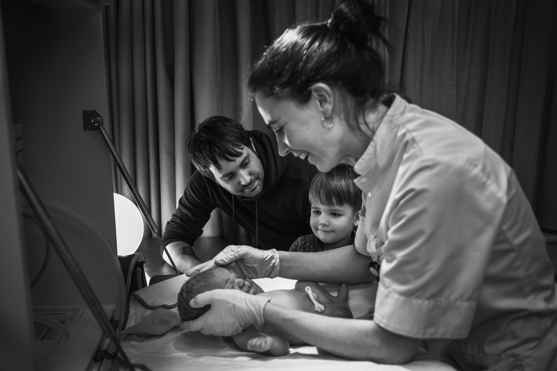 Een vrouw houdt een baby vast terwijl een man en een kind toekijken.