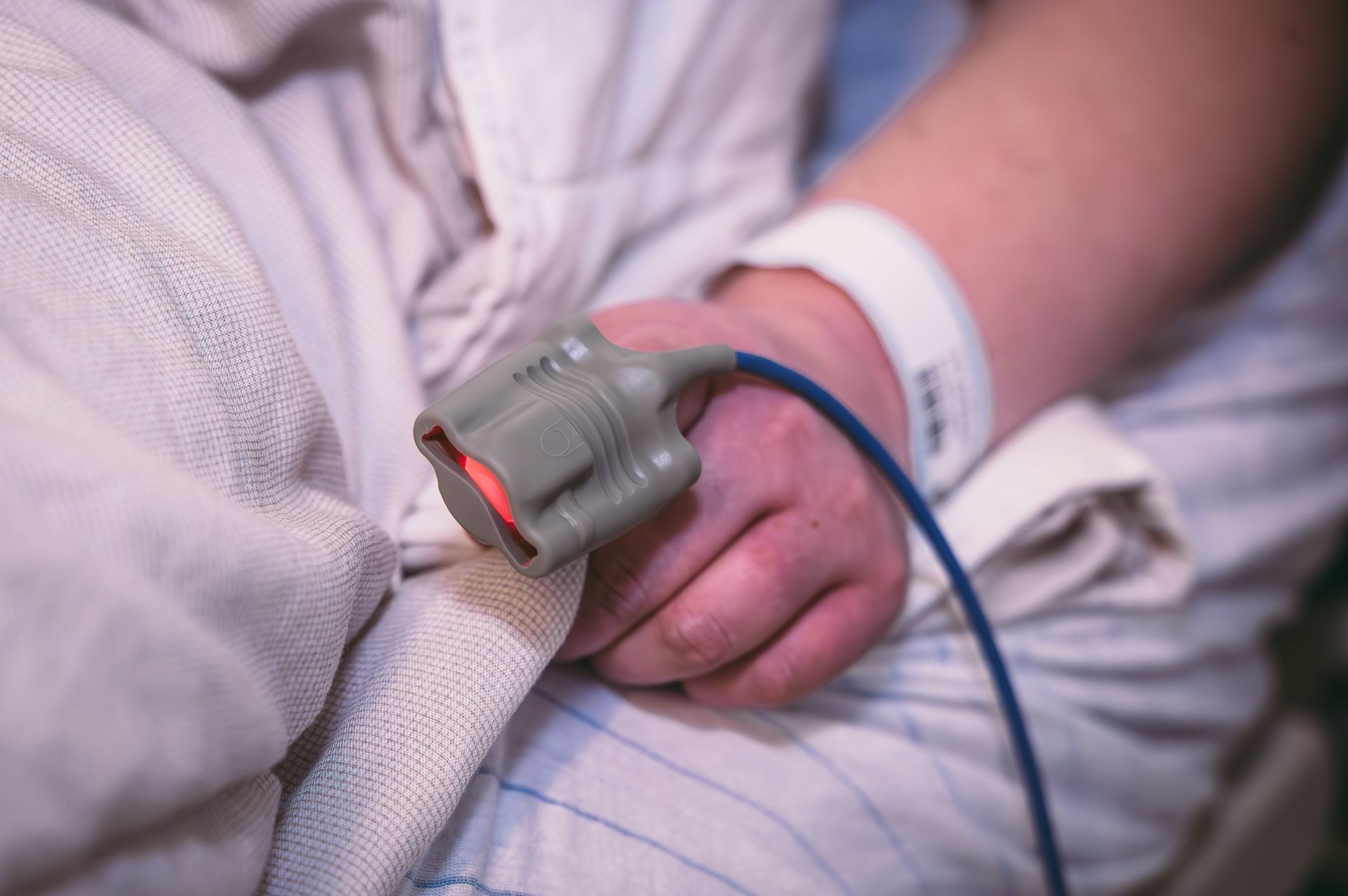 Een persoon in een ziekenhuisbed houdt een pulsoximeter in zijn hand.