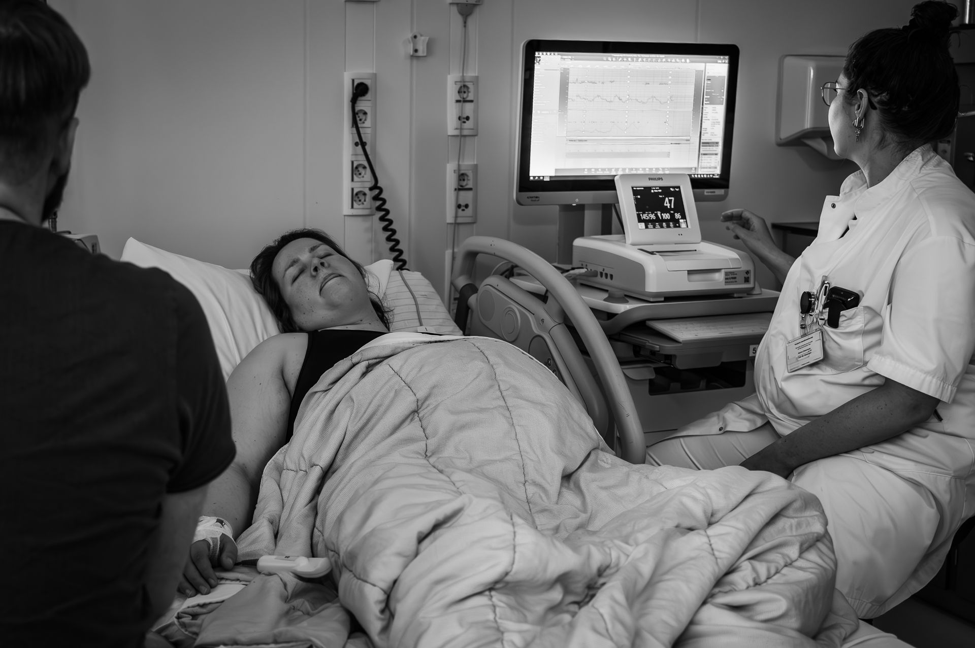 Een vrouw ligt in een ziekenhuisbed met een man en een verpleegster.