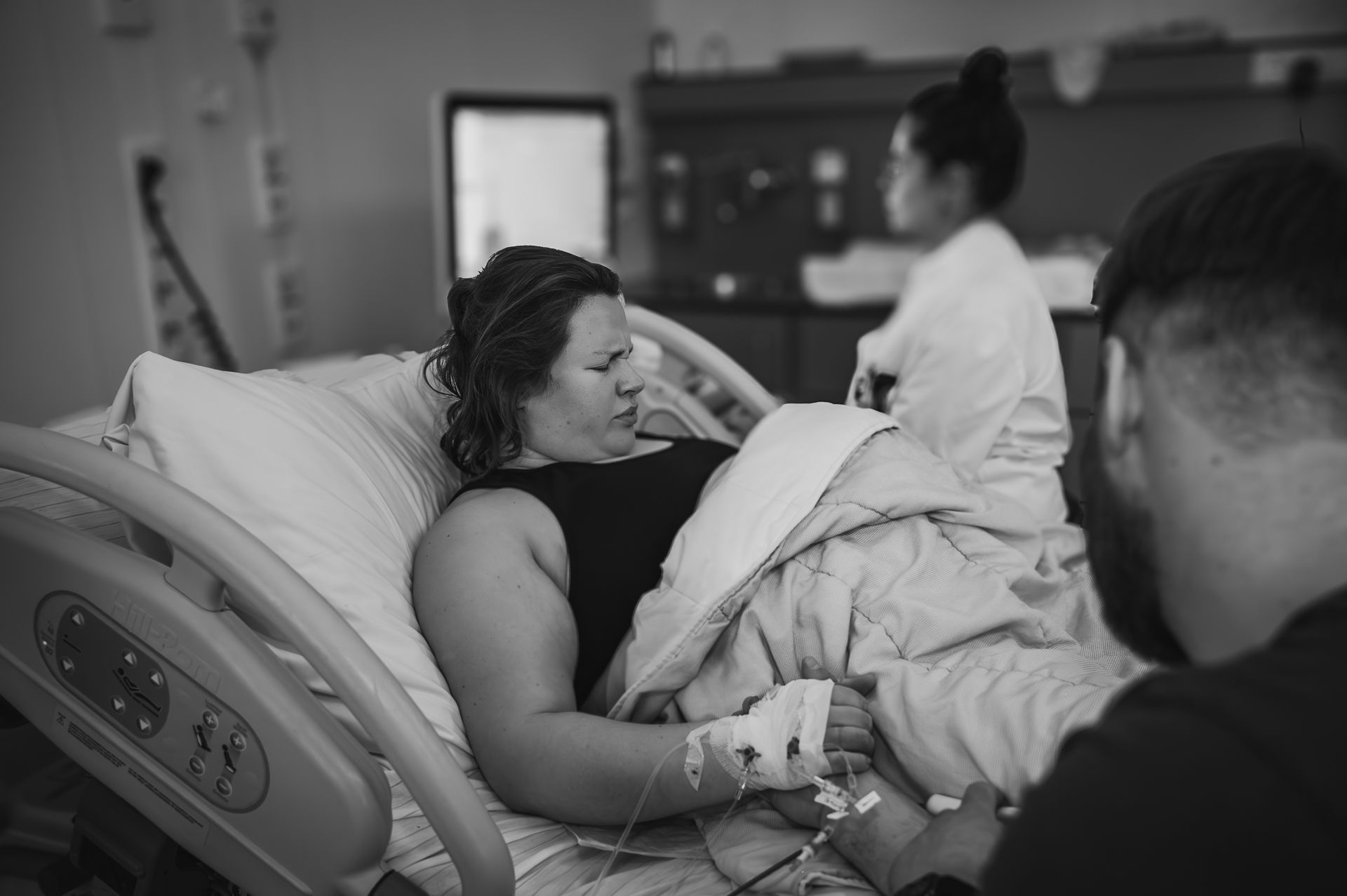 Een vrouw ligt in een ziekenhuisbed, terwijl een man haar hand vasthoudt.