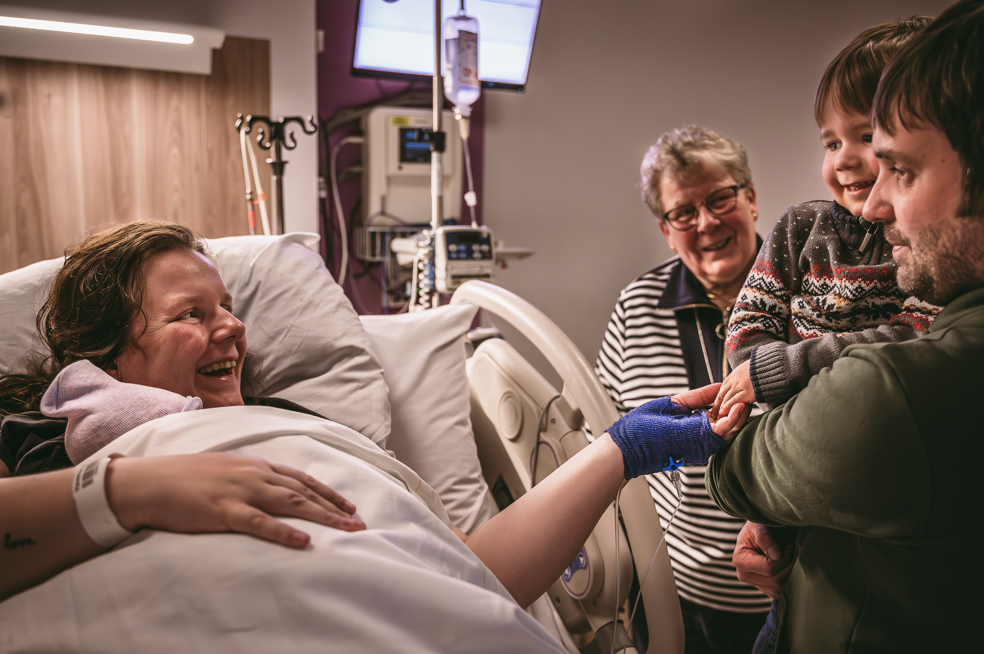 Een vrouw bevalt in een ziekenhuisbed terwijl haar familie toekijkt.