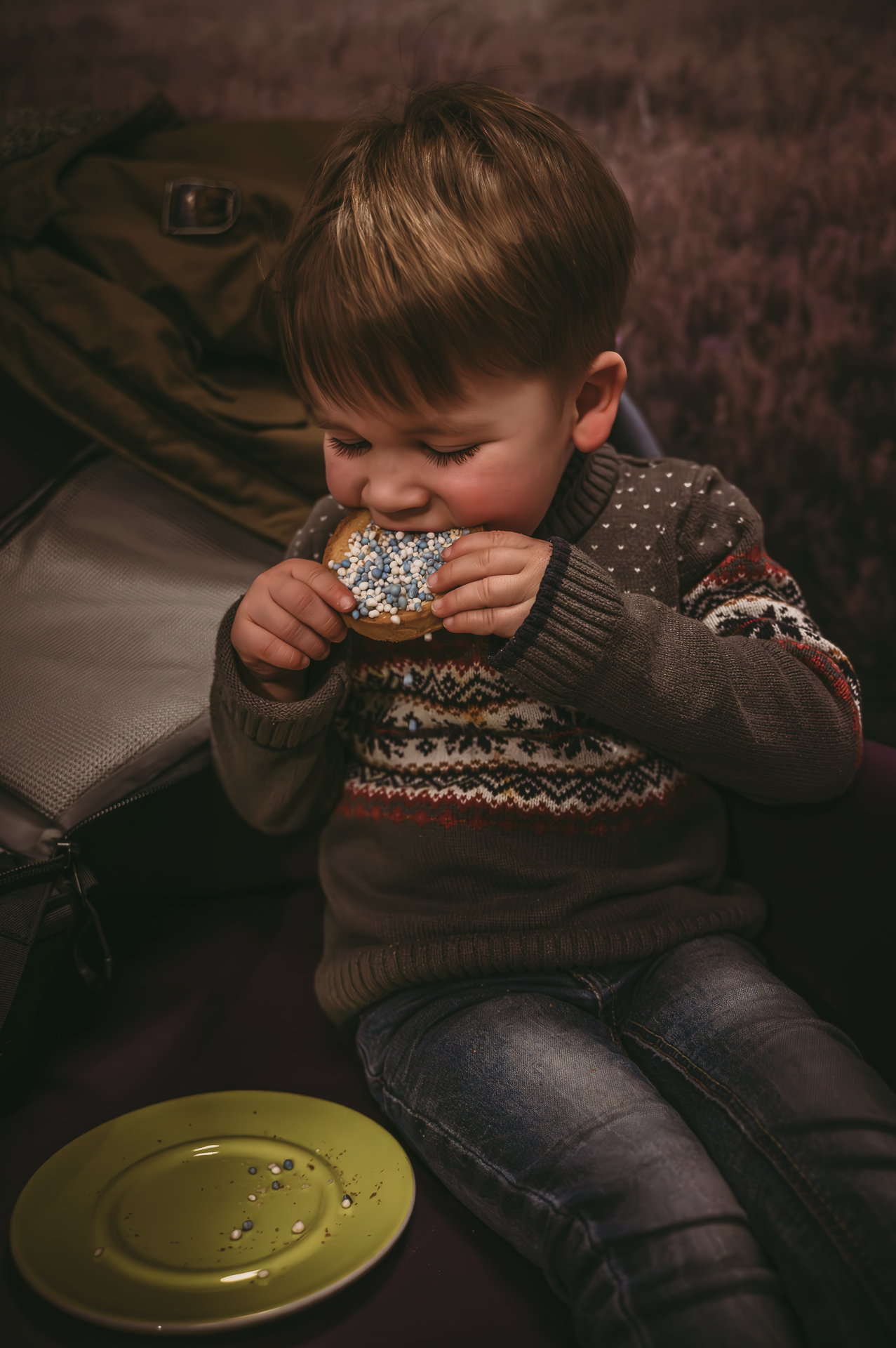 Een jonge jongen zit op een bank en eet een donut met hagelslag.