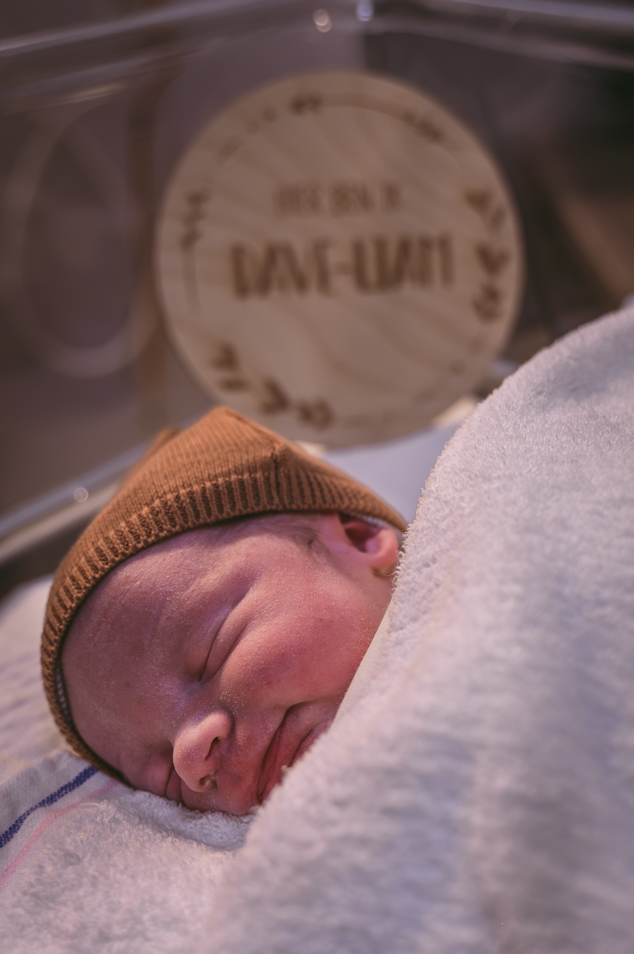 Een pasgeboren baby met een bruine muts slaapt in een couveuse.