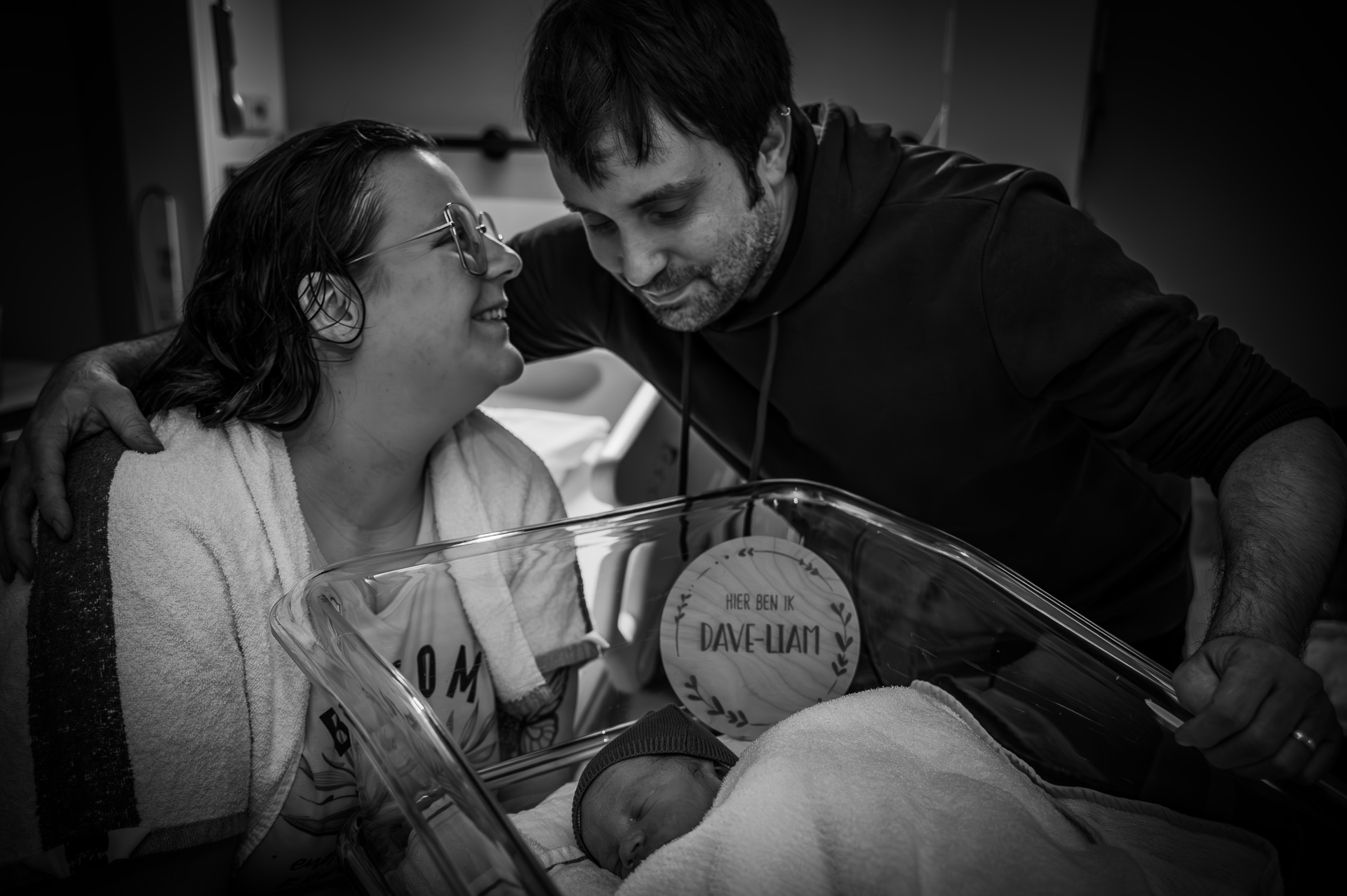 Een man en een vrouw houden een pasgeboren baby vast in een ziekenhuisbedje.