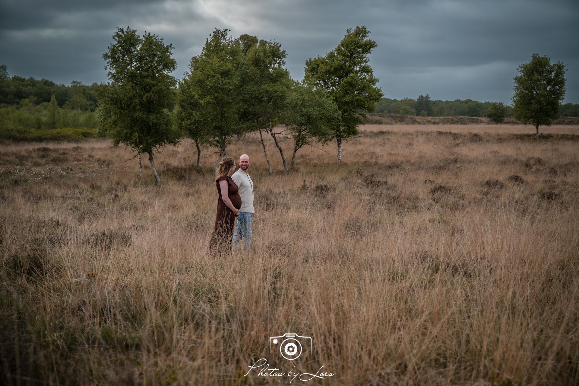 Een man zit naast een zwangere vrouw op een zandstrand.