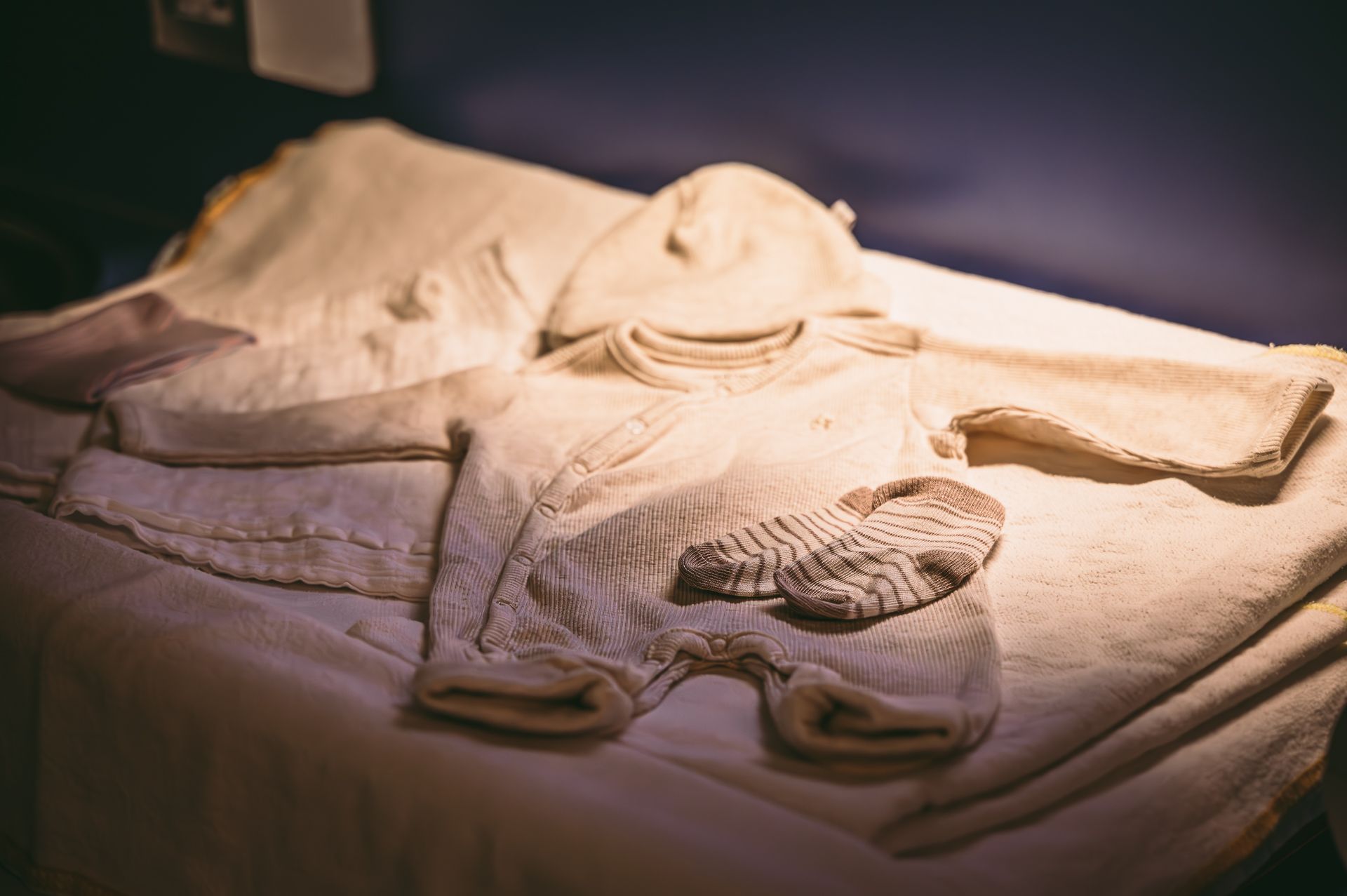 De kleertjes van een baby liggen op een bed.