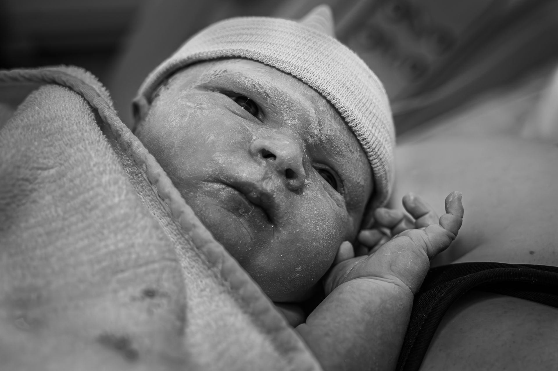 Een zwart-witfoto van een pasgeboren baby met een hoedje op.