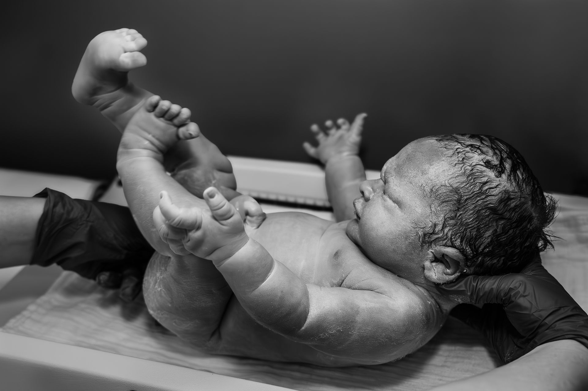 Een zwart-witfoto van een pasgeboren baby die op een tafel ligt.