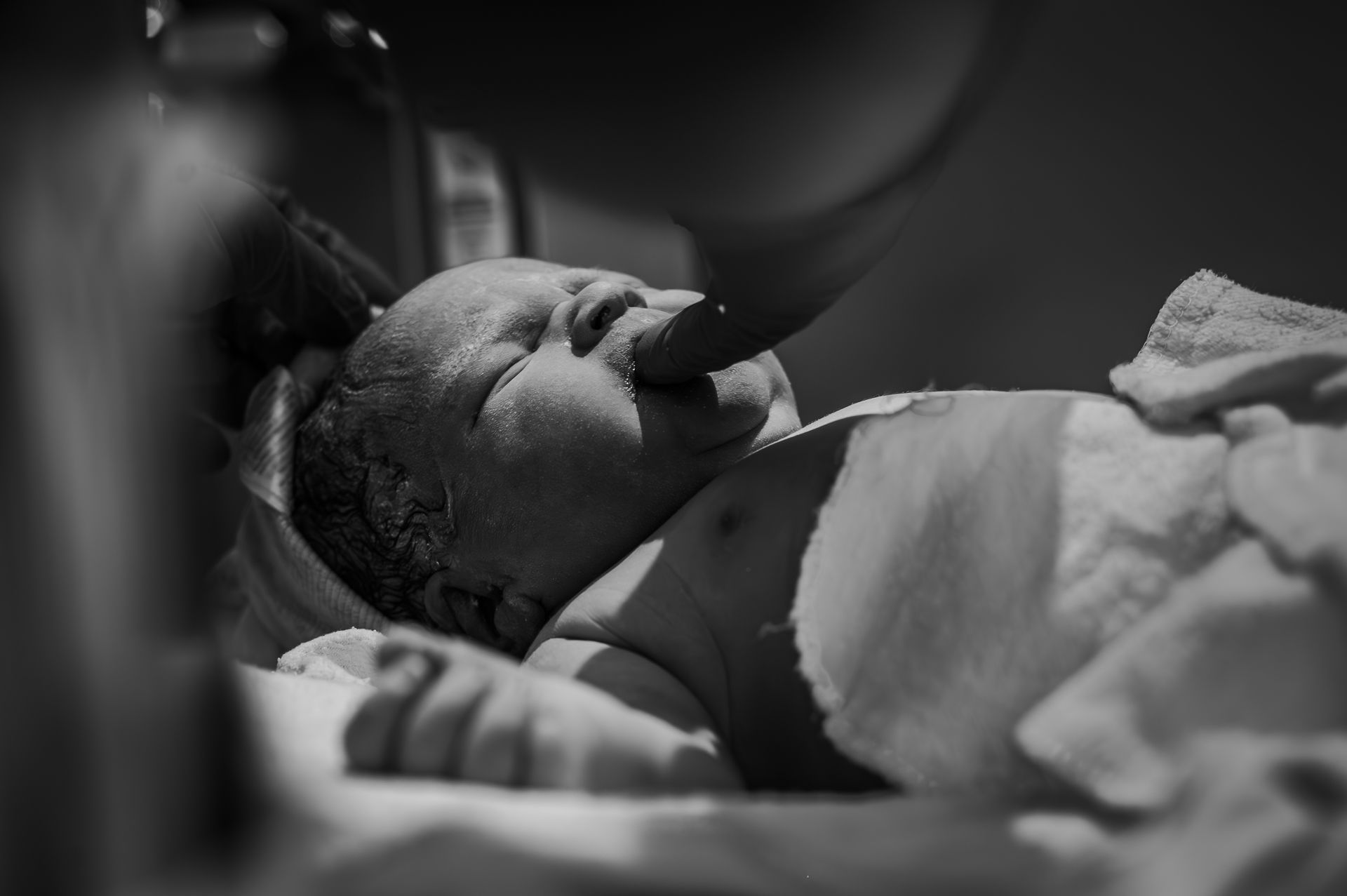 Een zwart-witfoto van een pasgeboren baby die op een bed ligt.