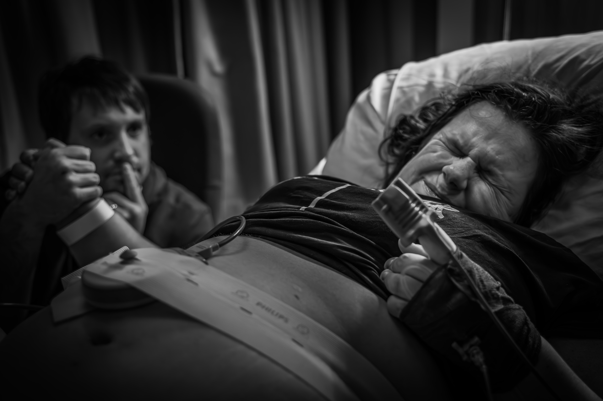 Een man houdt de hand van een zwangere vrouw vast in een ziekenhuisbed.