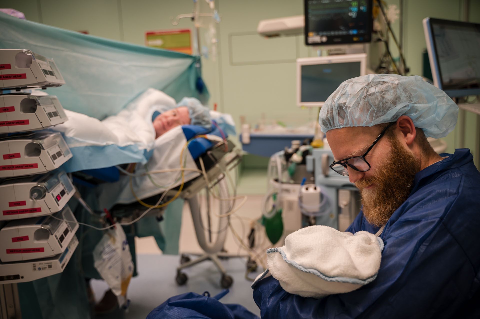 Een man houdt een baby vast in een operatiekamer terwijl er een baby wordt geopereerd.