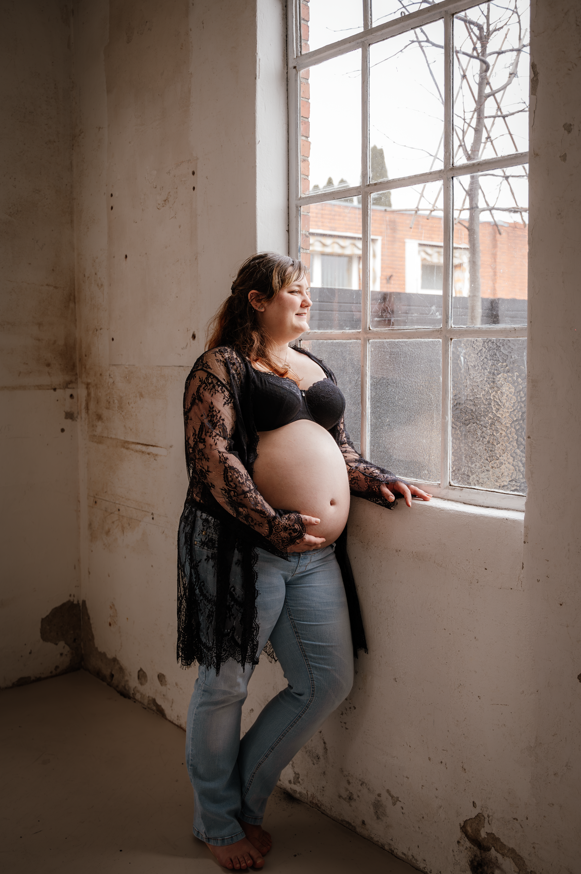 Een zwangere vrouw leunt tegen een raam in een kamer.