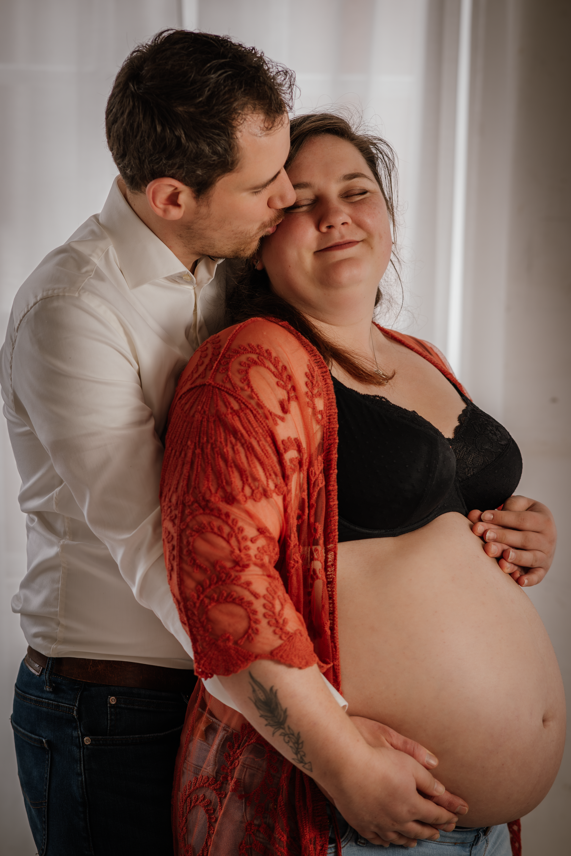 Een man kust een zwangere vrouw op het voorhoofd.