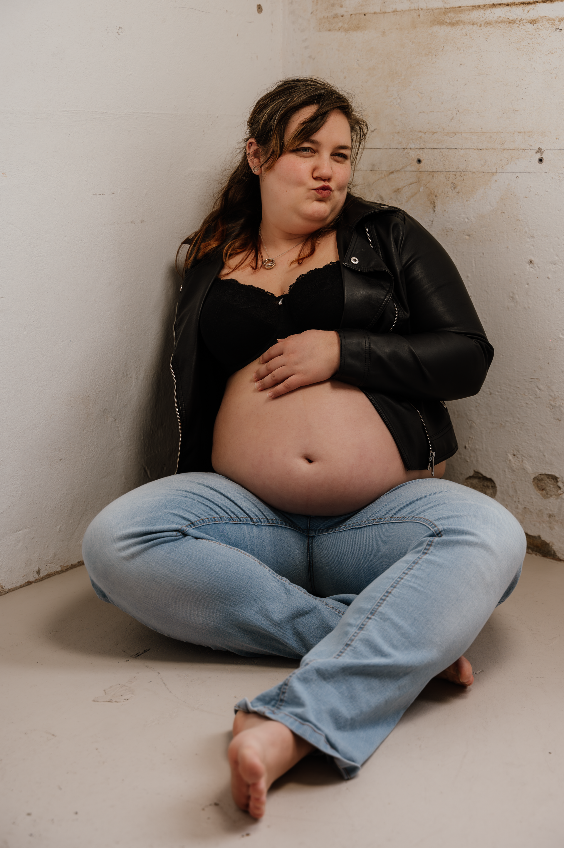 Een zwangere vrouw zit op de grond met haar benen gekruist.