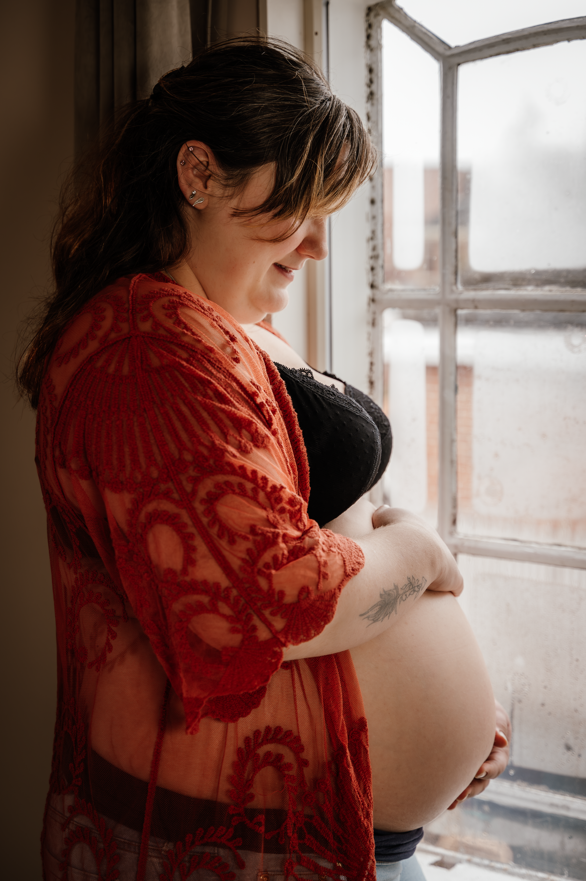 Een zwangere vrouw staat voor een raam en houdt haar buik vast.