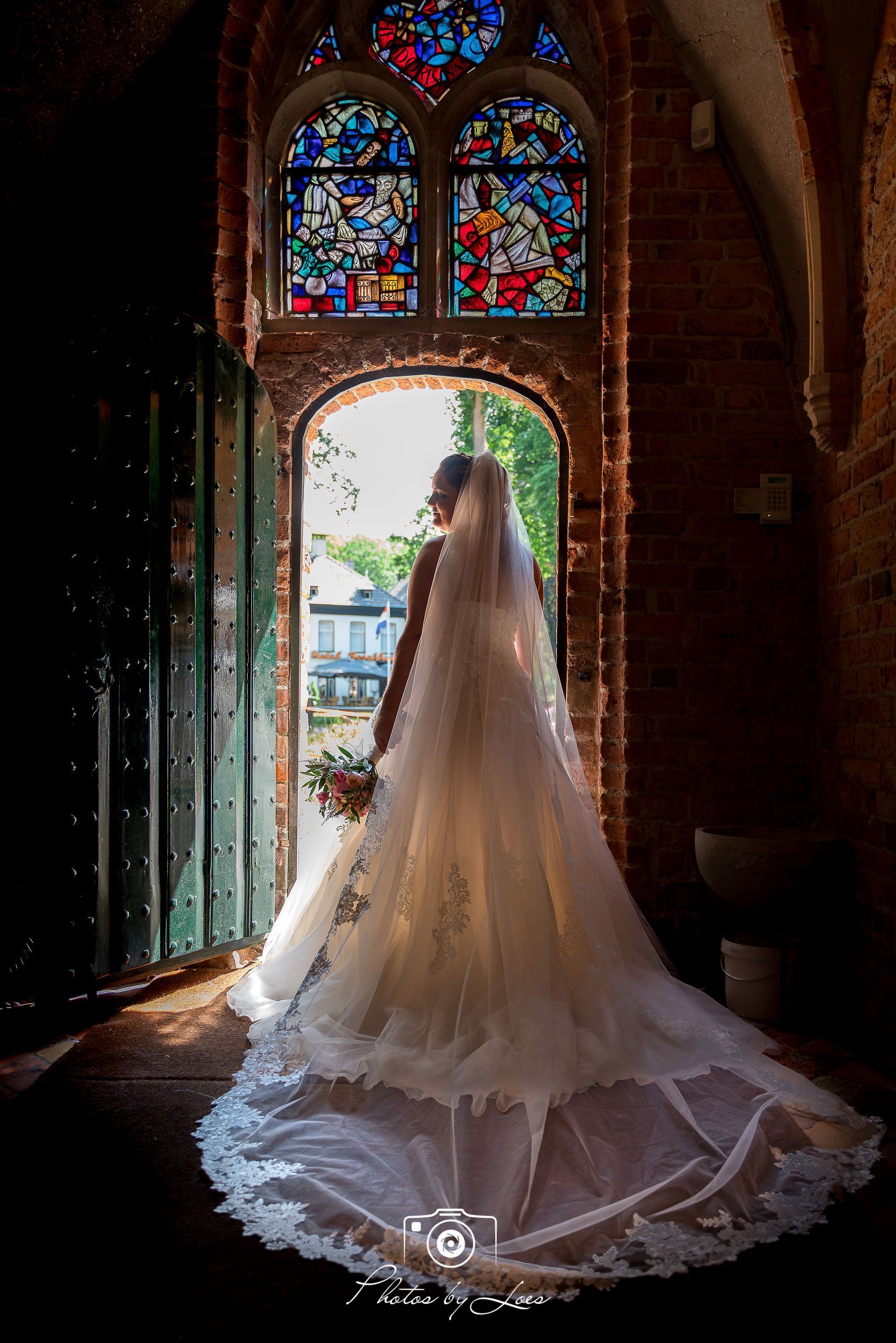 Een bruid in een trouwjurk staat voor een glas-in-loodraam.