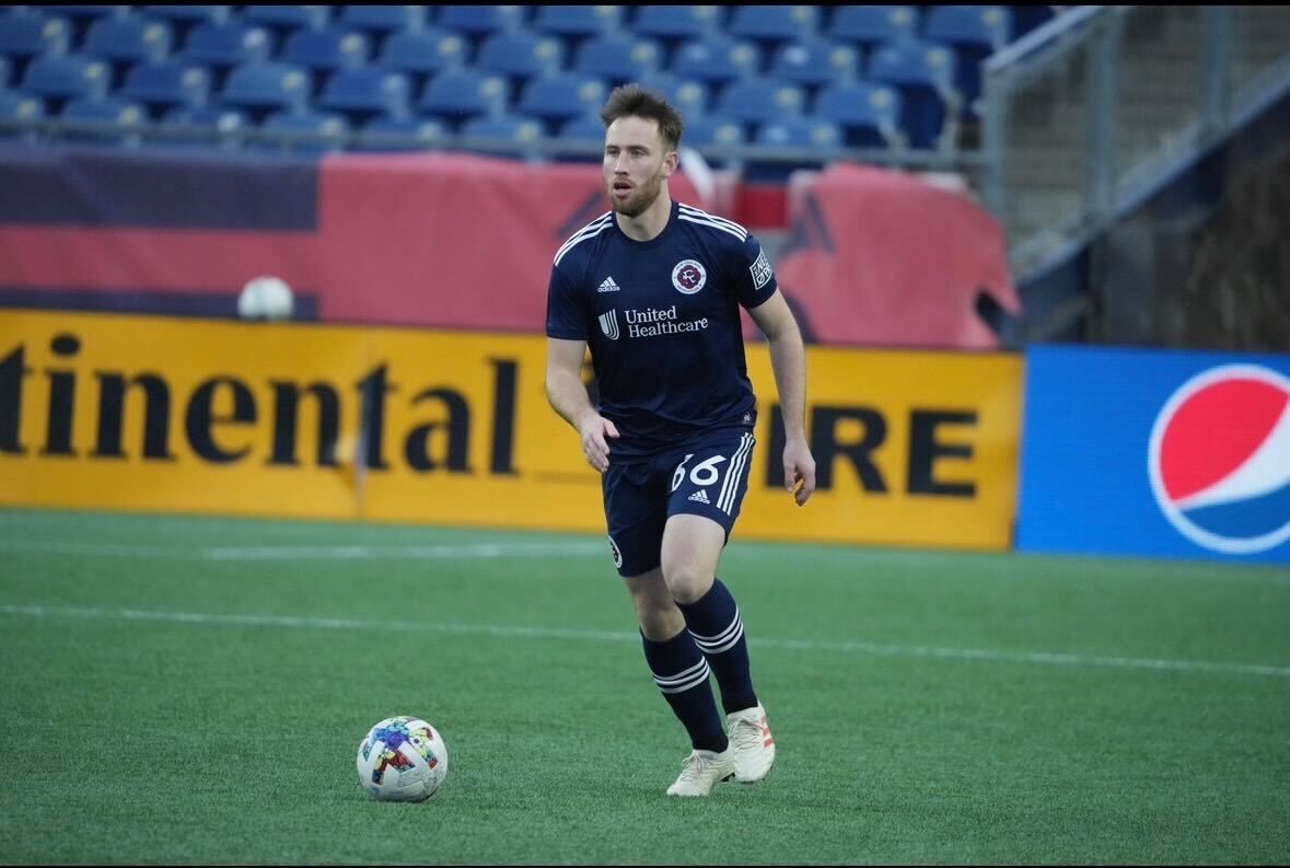 A soccer player in a dark blue uniform dribbles a soccer ball on a field in front of Continental and Pepsi signage.