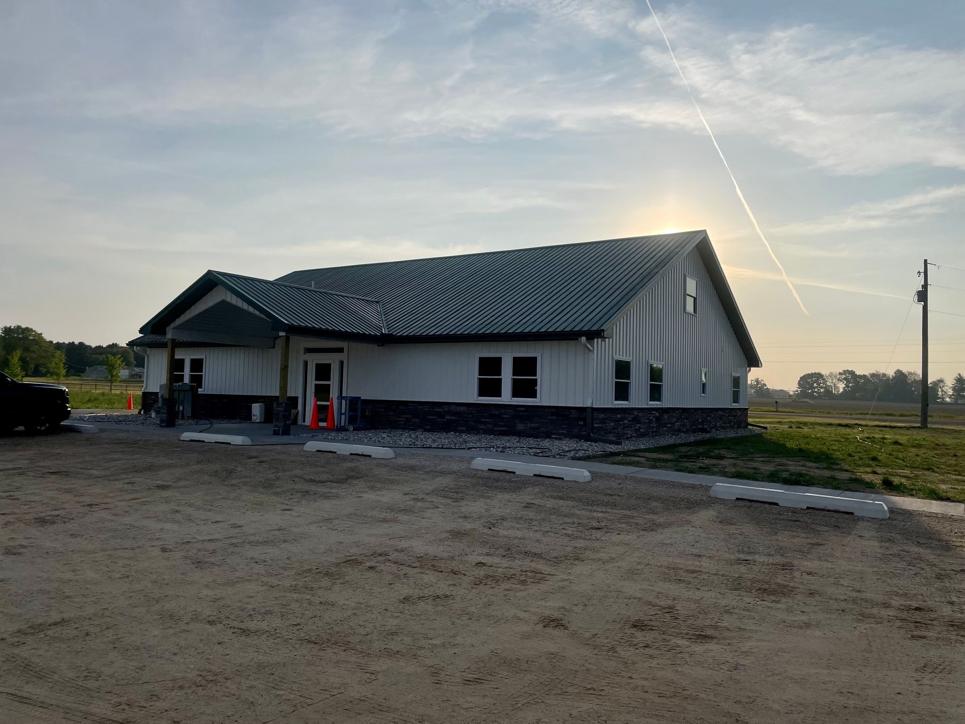 A large white building with a green roof is sitting in the middle of a dirt field.