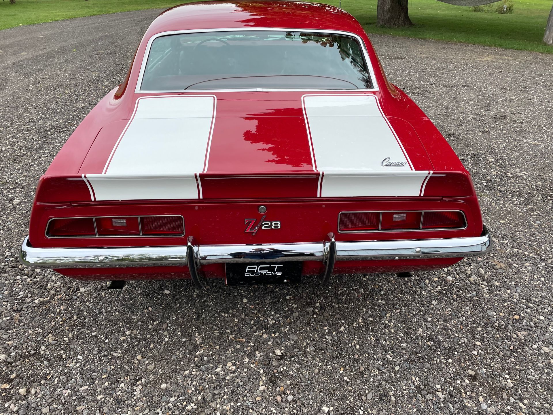 A red and white chevrolet camaro is parked on a gravel road.