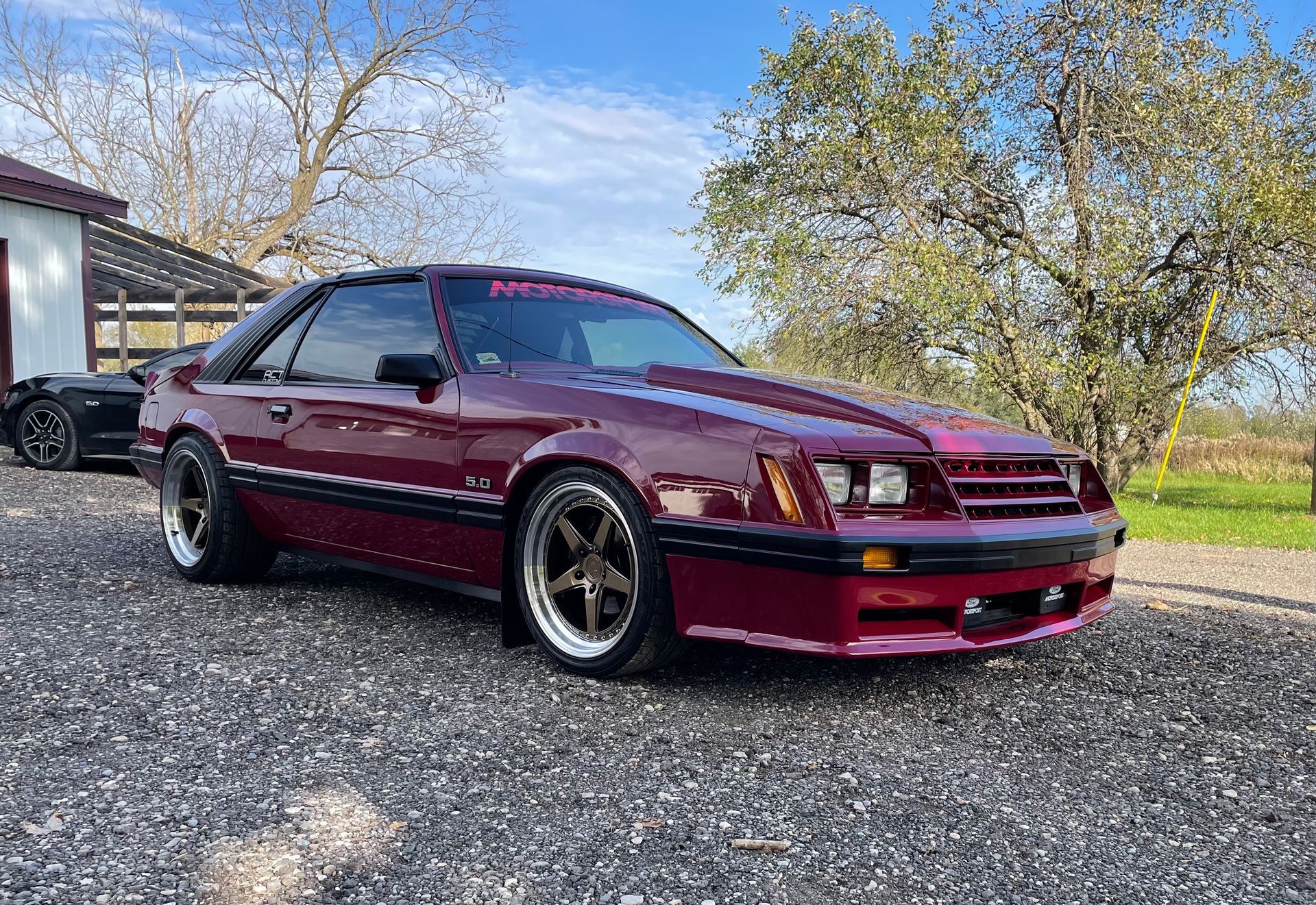 A red ford mustang is parked in a gravel lot.