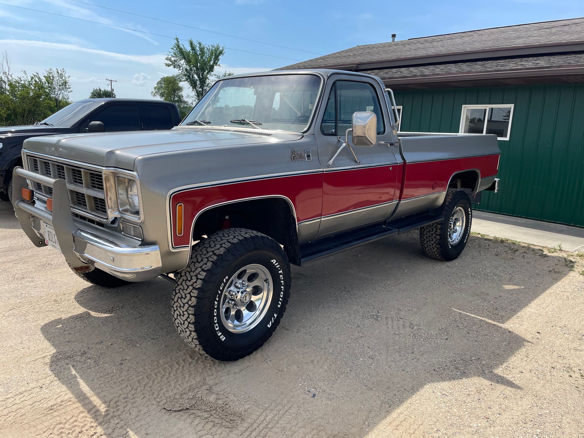 A silver and red pickup truck is parked in front of a green building.